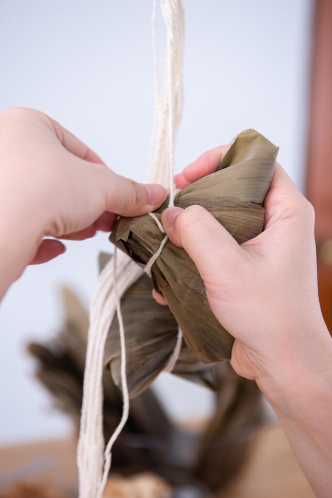 Rice dumpling zongzi making – wrapping Chinese rice dumpling zongzi on table at home for Dragon Boat Festival celebration, close up, lifestyle. Stock Free