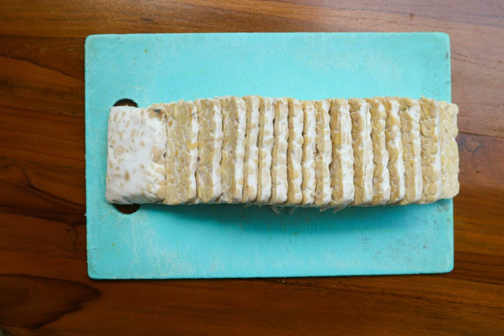 Sliced fresh raw tempeh, on a plastic cutting board on a wooden background. Food preparation concept Stock Free