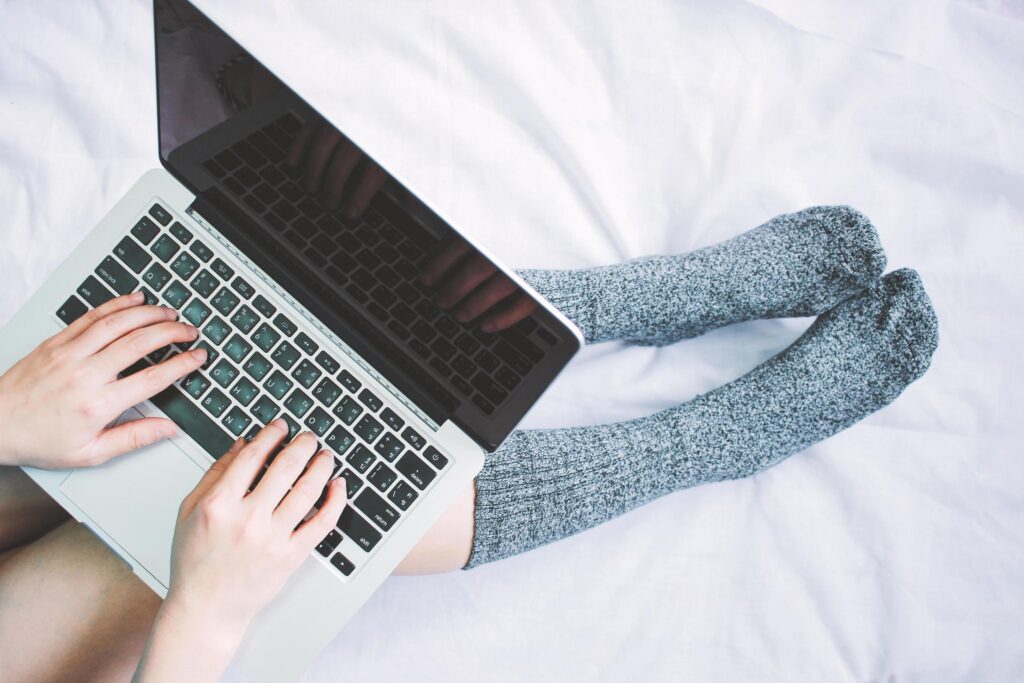 Top view of woman legs in socks and using laptop on cozy bed, lifestyle concept Stock Free