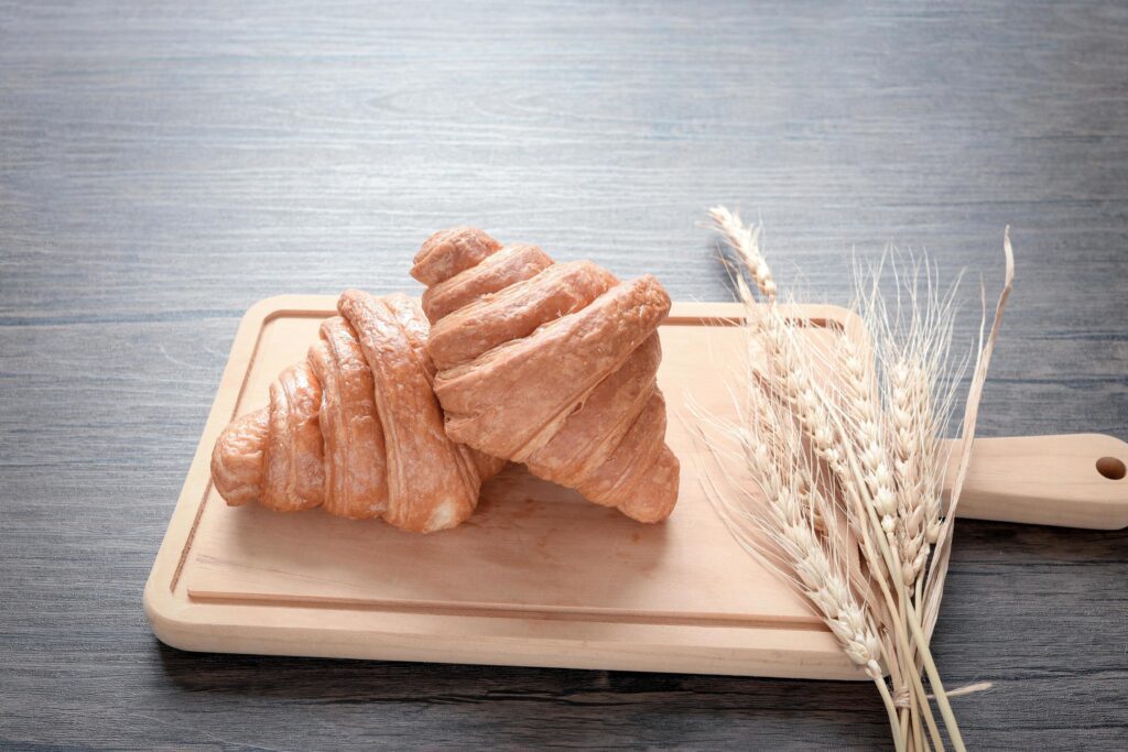 Two freshly baked delicious croissants with spikelets on wooden cutting board, food on breakfast table Stock Free