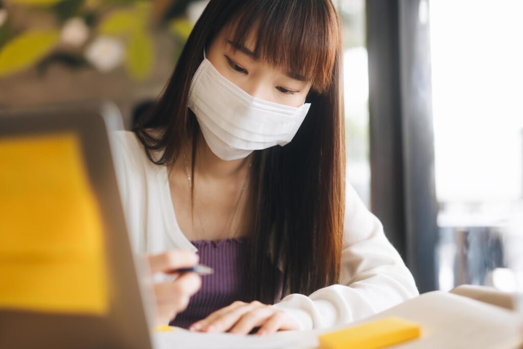 Young adult asian female with protective face mask work and study at cafe new normal lifestyle. Stock Free