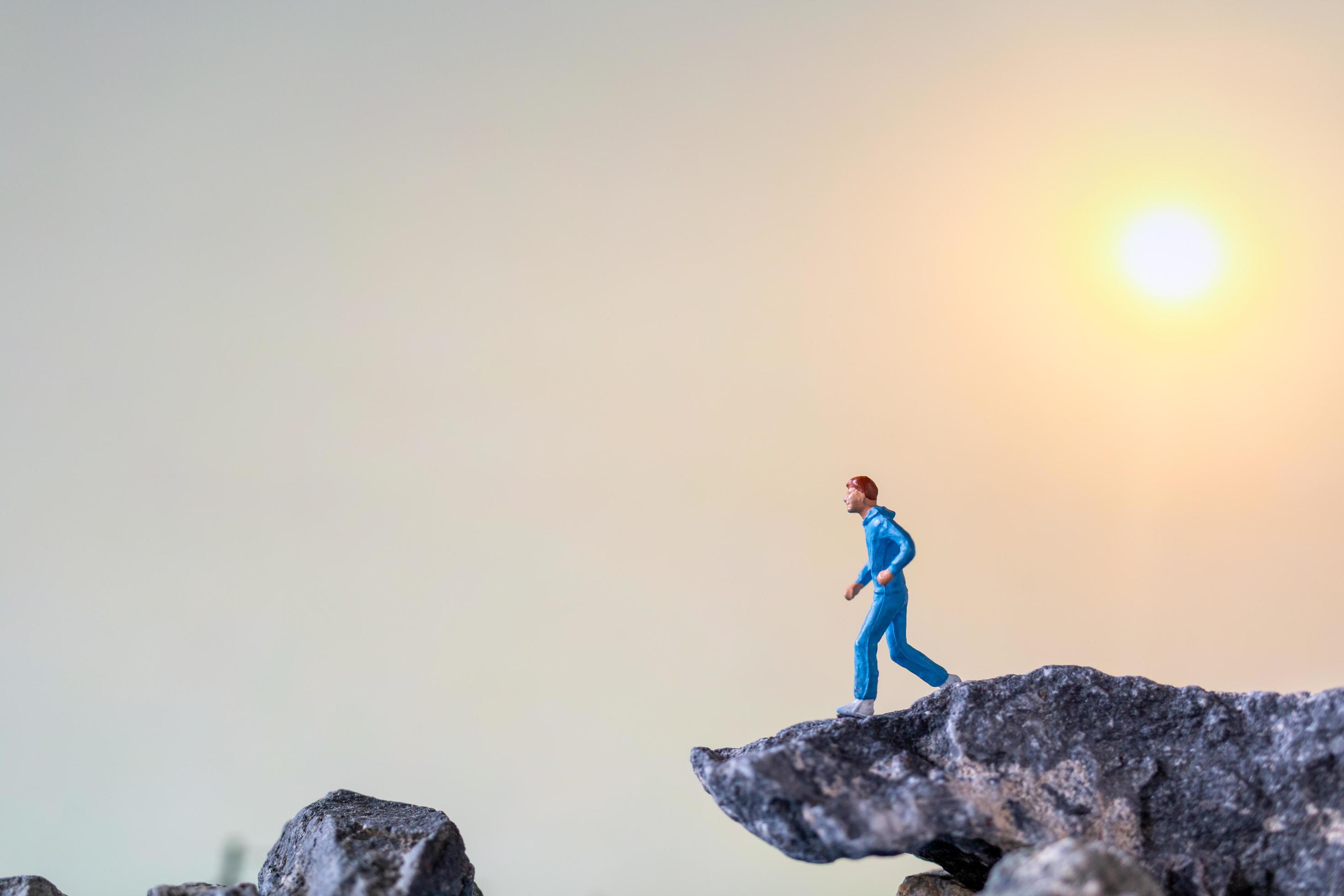 Miniature people running on a rock cliff with nature background, health and lifestyle concept Stock Free