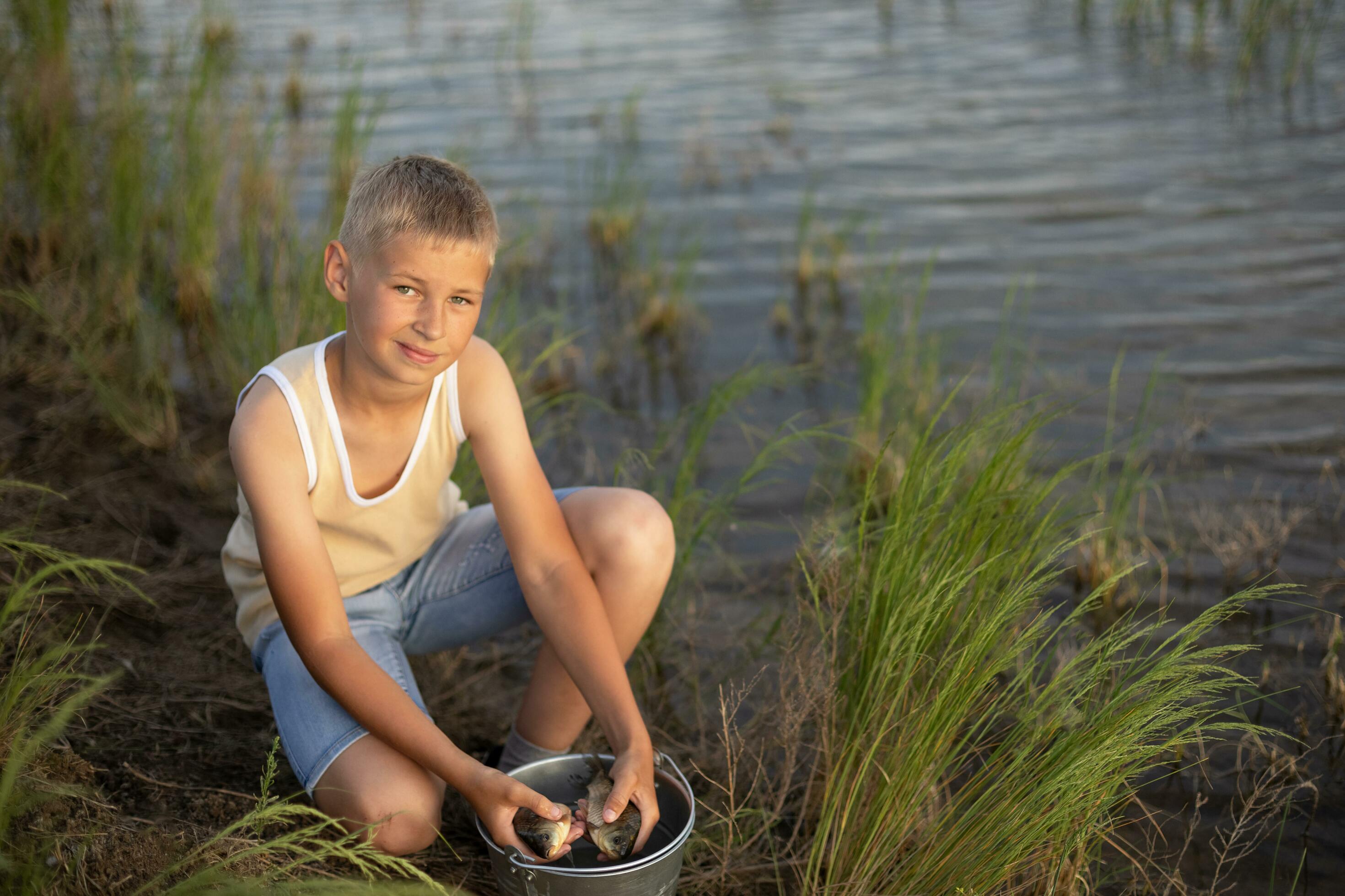 Little boy is fishing at sunset on the lake. Summer holidays in a village. Rest in nature, away from the city Stock Free