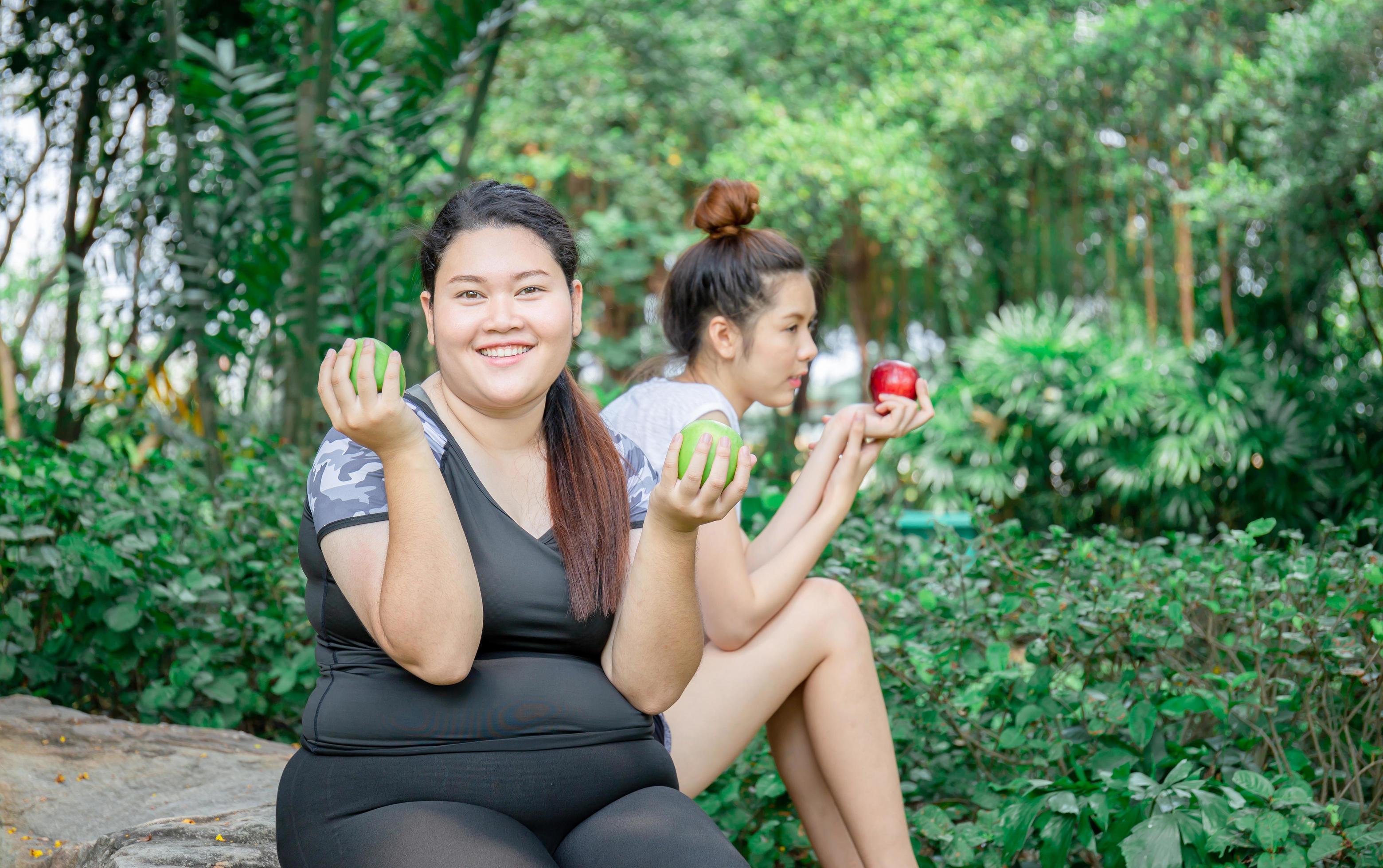 Smiling young women holding an apple sitting relax in the park, healthy and lifestyle concept Stock Free