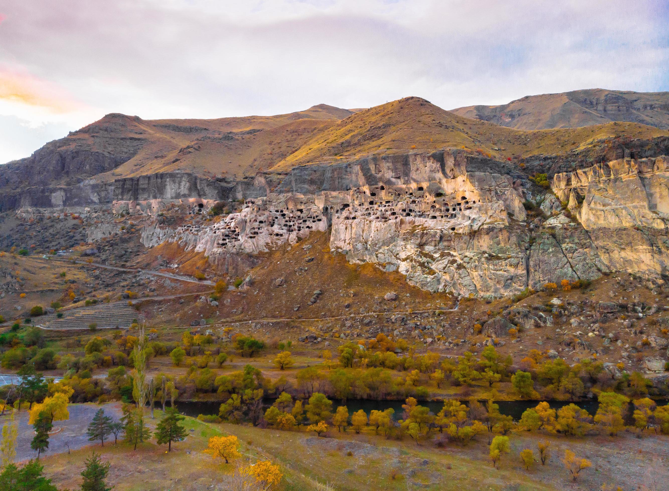 Aerial perspective of Vardzia-cave city from above with paravani river and autumn nature in foreground. Historical unesco sites Georgia. Stock Free