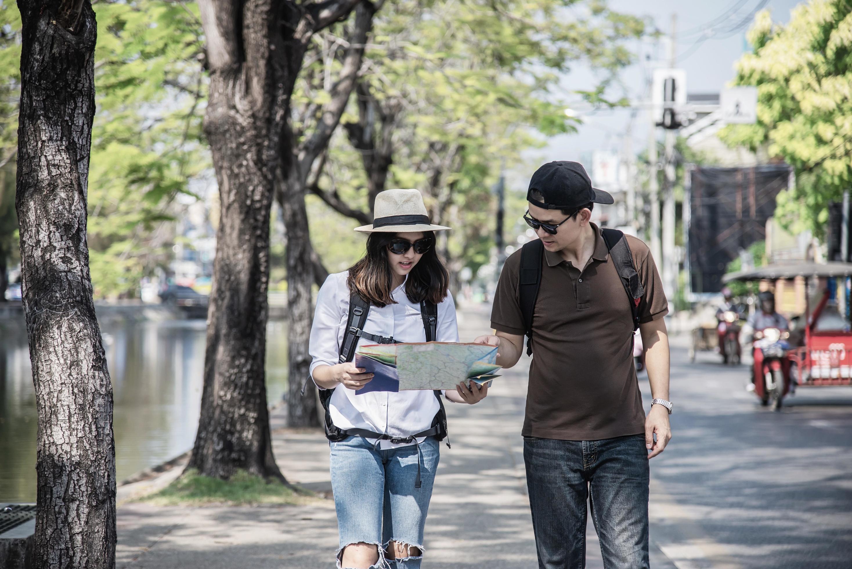 Asian backpack couple tourist holding city map crossing the road – travel people vacation lifestyle concept Stock Free