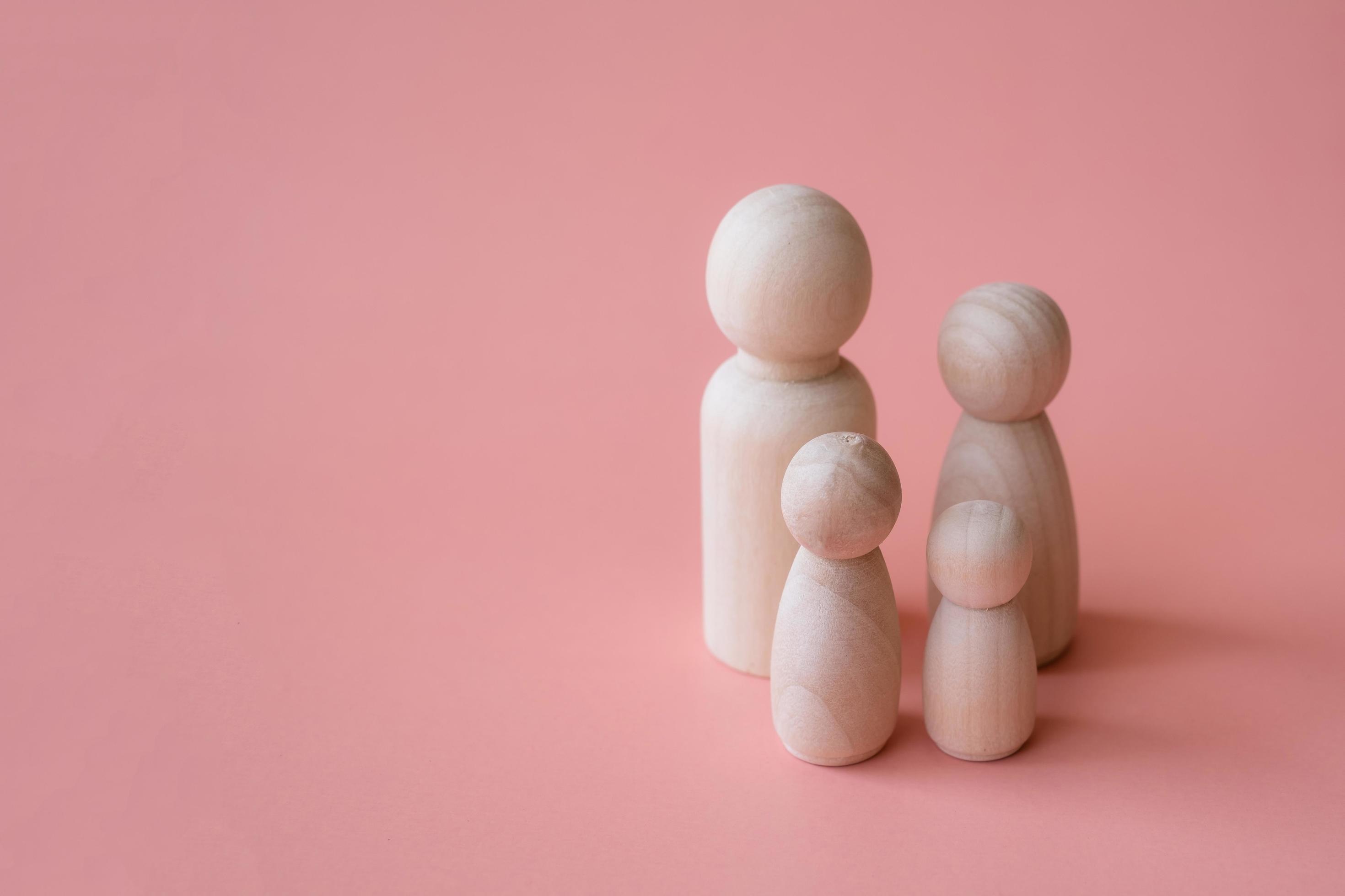 Wooden figurines of family father, mother and children on pink background. A warm family concept. Stock Free