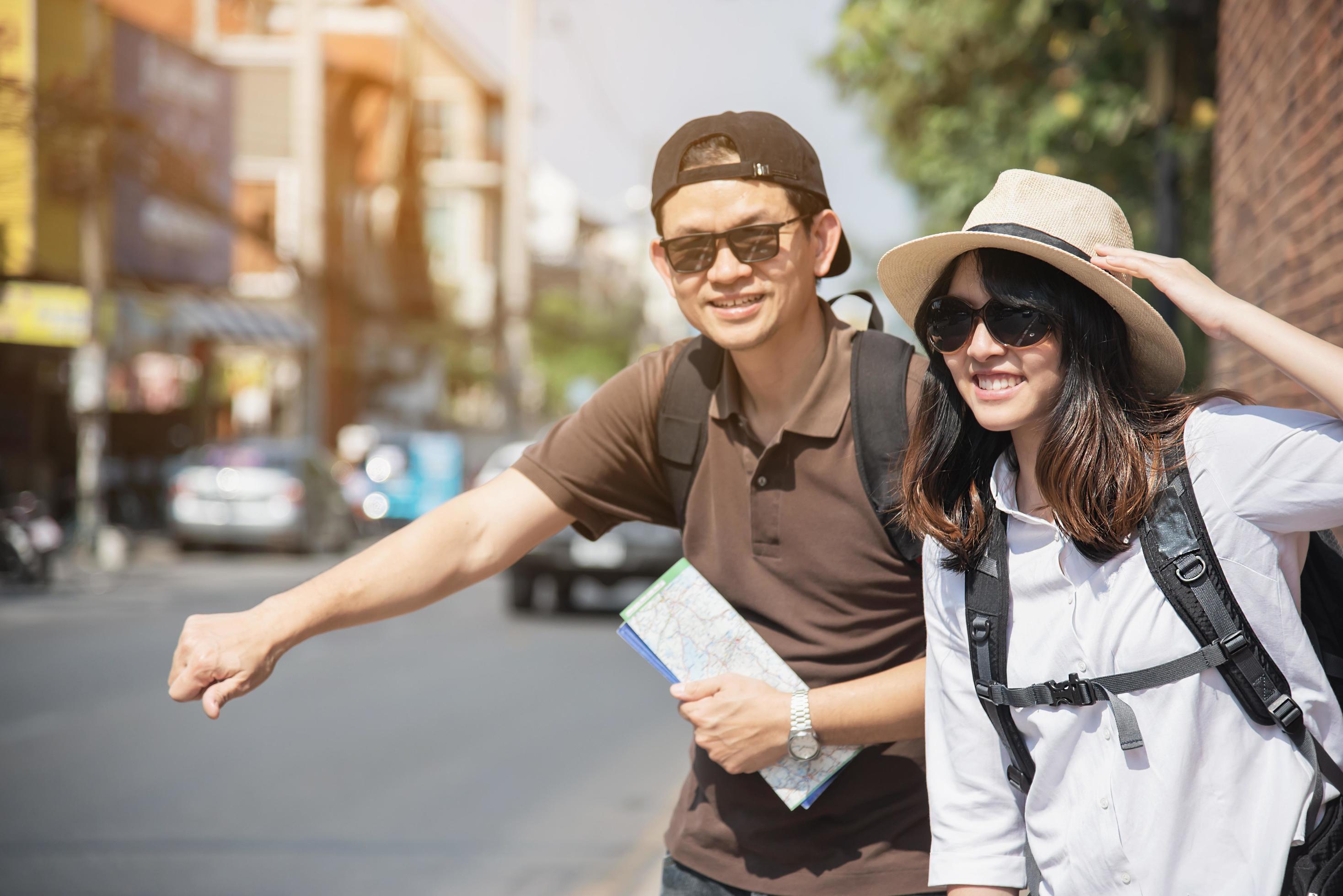 Asian backpack couple tourist holding city map crossing the road – travel people vacation lifestyle concept Stock Free