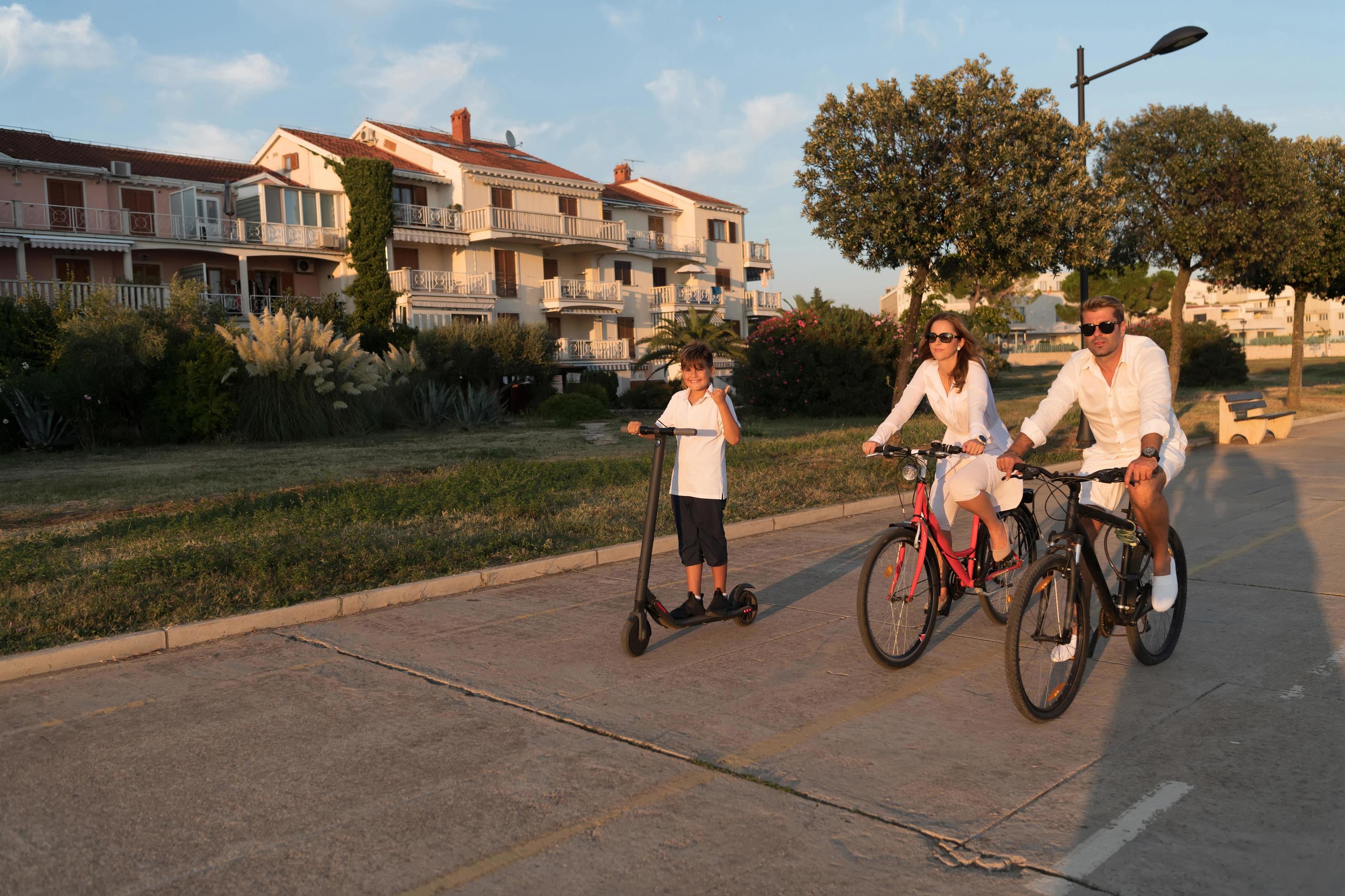 Happy family enjoying a beautiful morning by the sea together, parents riding a bike and their son riding an electric scooter. Selective focus Stock Free