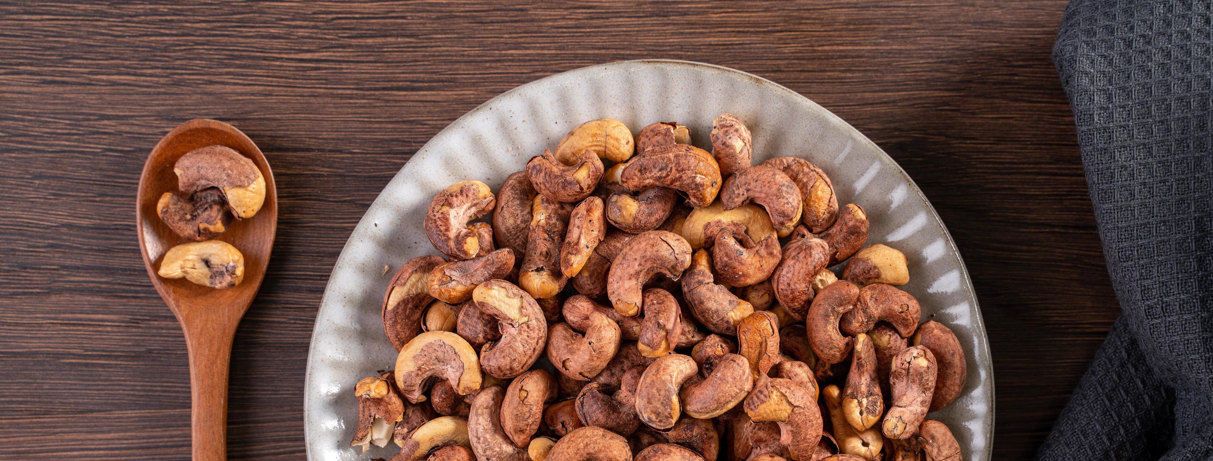 Cashew nuts with peel in a plate on wooden tray and table background, healthy raw food plate. Stock Free