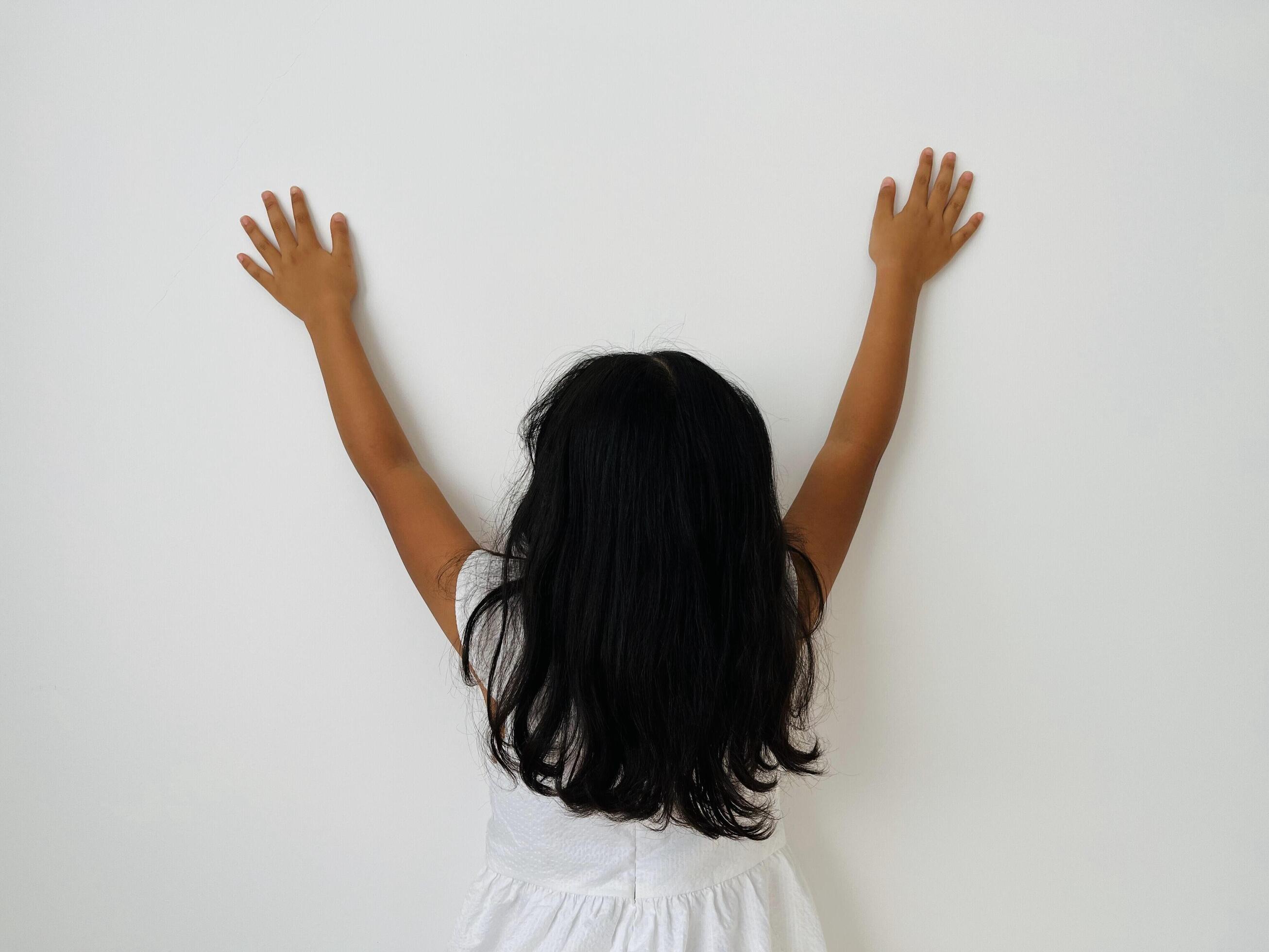 A five years old Asian child with long hair facing away from the camera with both hands raised upwards, copy space for text and advertisement Stock Free