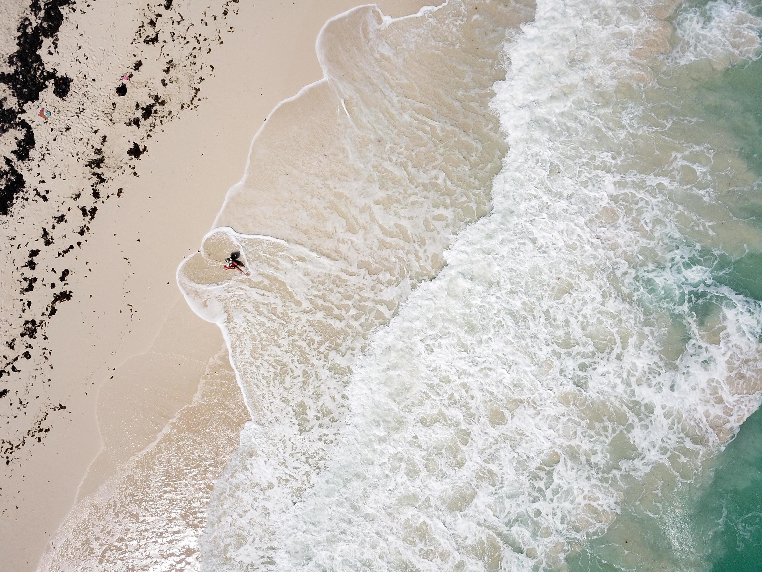 Aerial view of the beach, waves making a heart shape around a woman in the hat Stock Free