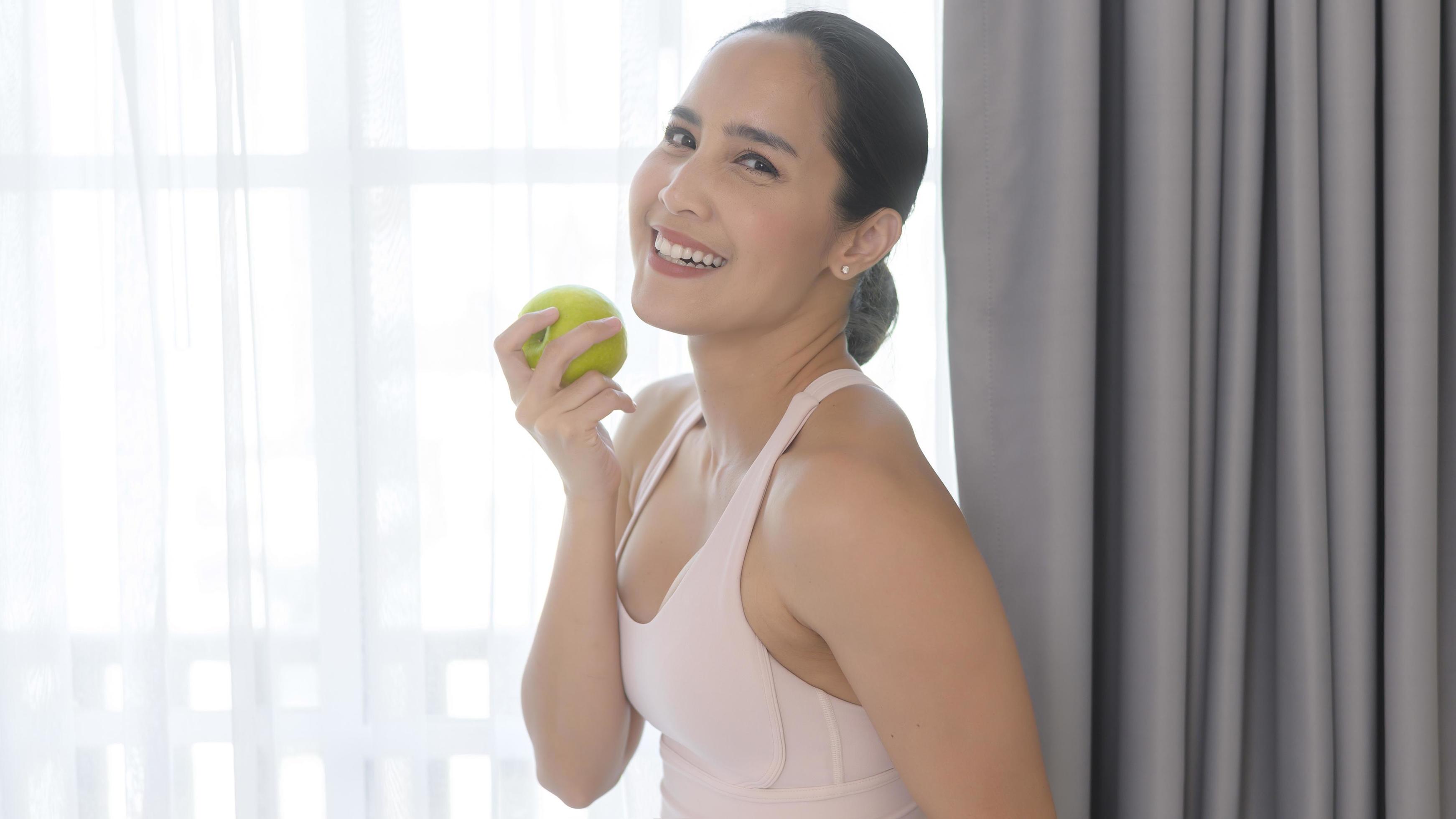 Fit young woman eating an apple after work out at home, sport and healthy lifestyle concept. Stock Free