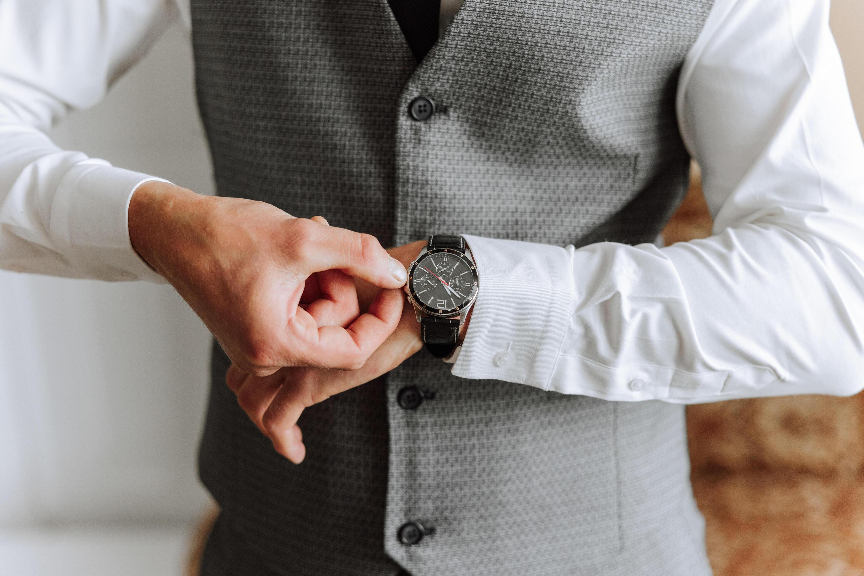 A man in a business suit is adjusting his wristwatch, a mug of coffee is on the table in his room. Close-up photo of a wristwatch. Stock Free