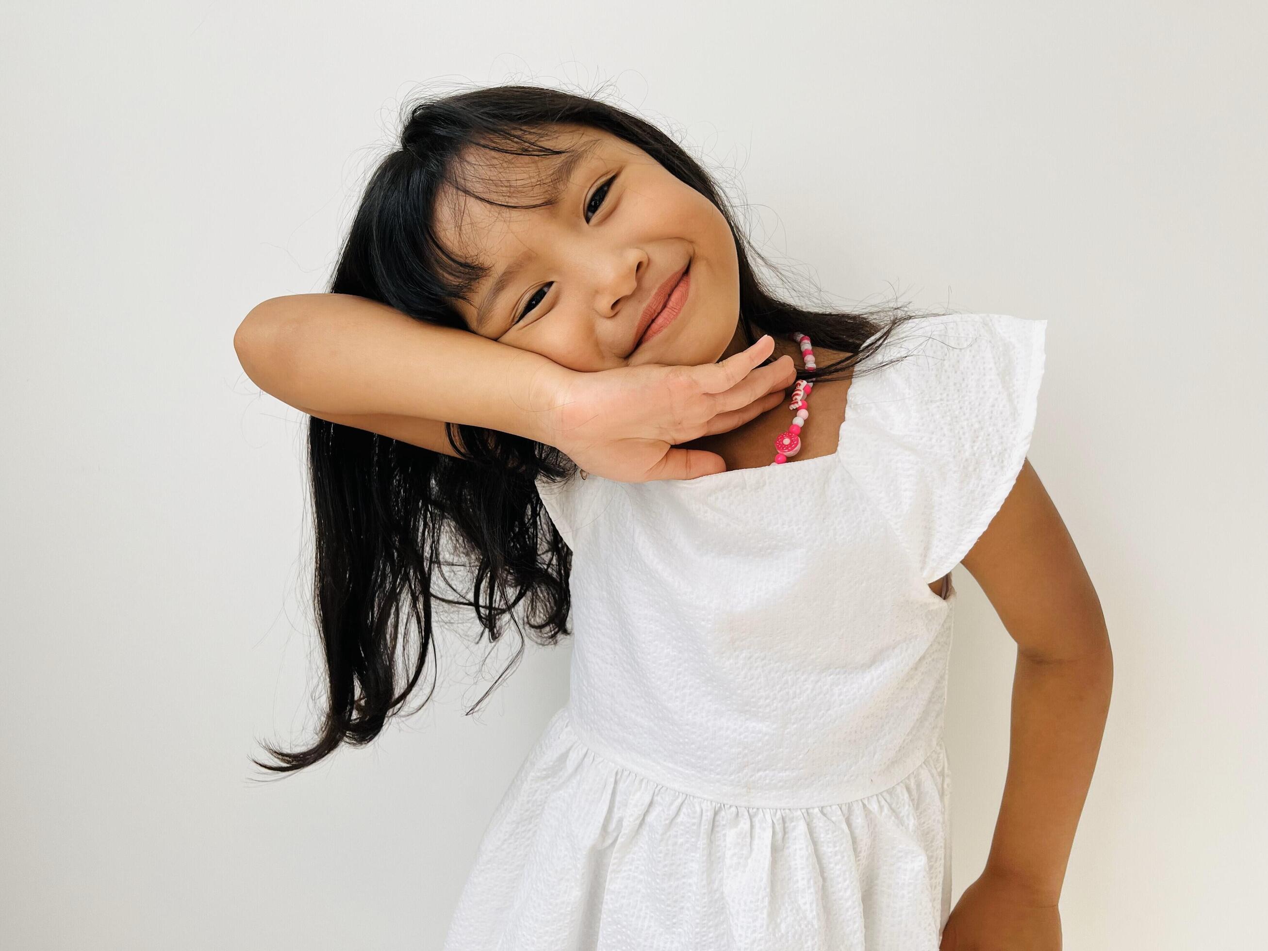 A cute Asian wavy black hair girl in cute poses. Five year old little girl wearing a white dress cheerfully smiles Stock Free