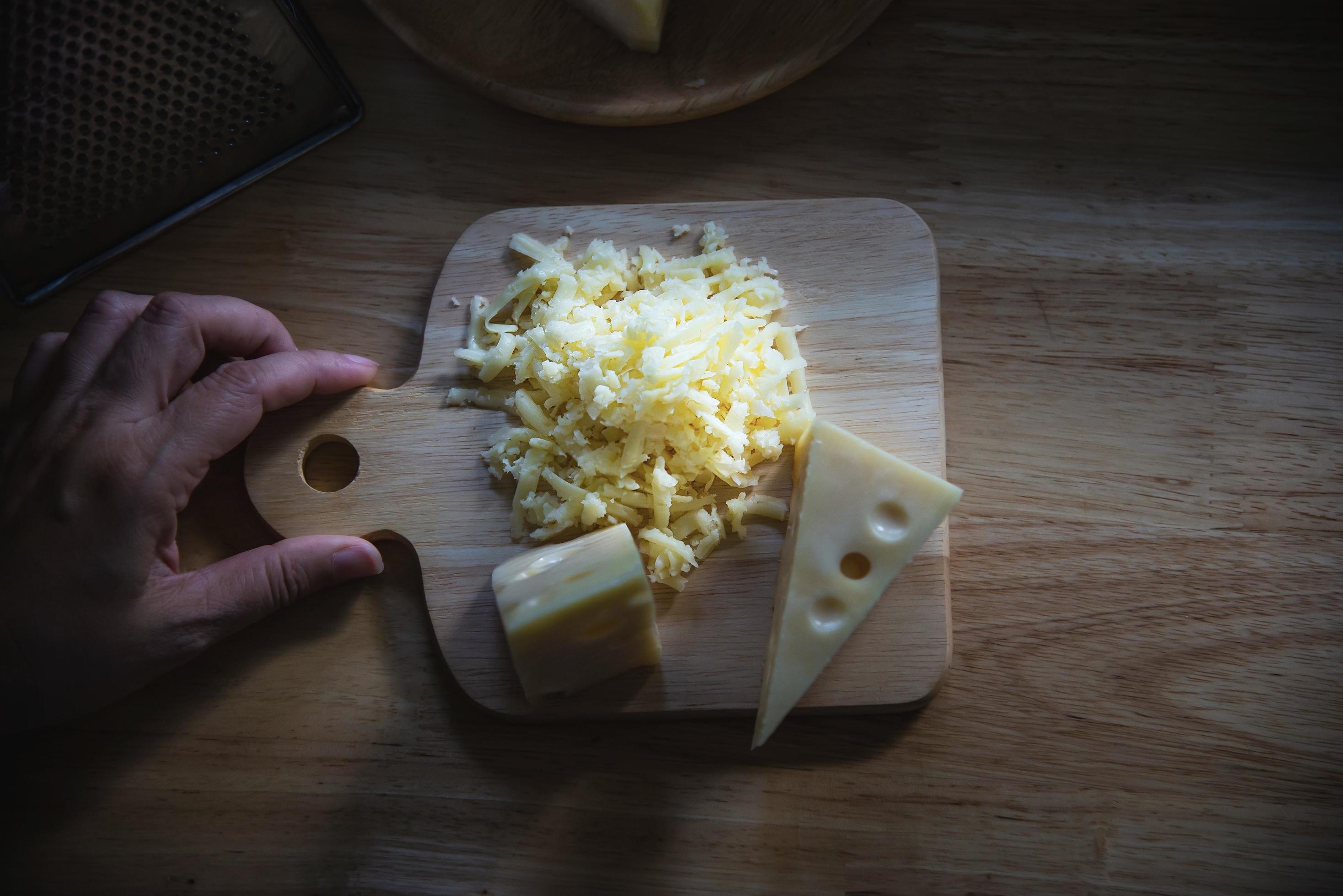 Woman preparing cheese for cook using cheese grater in the kitchen – people making food with cheese concept Stock Free