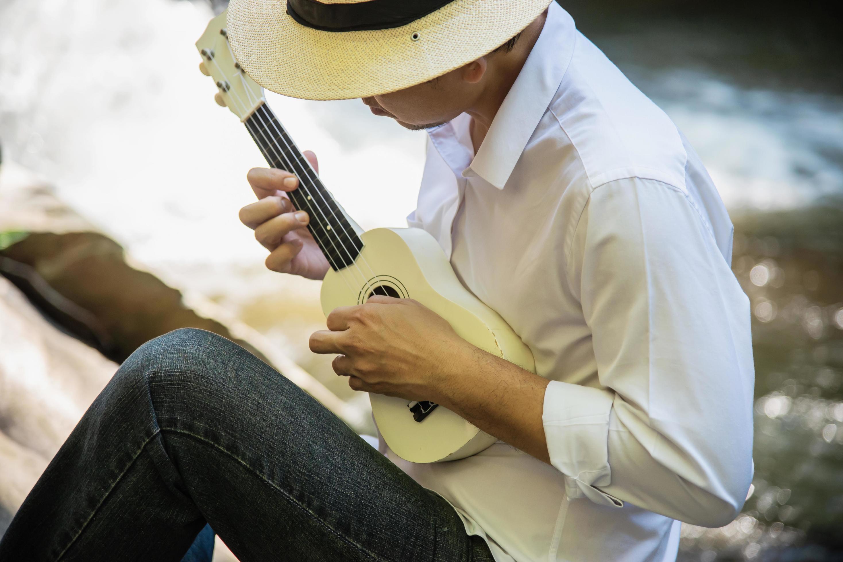 Man play ukulele new to the river- people and music instrument life style in nature concept Stock Free