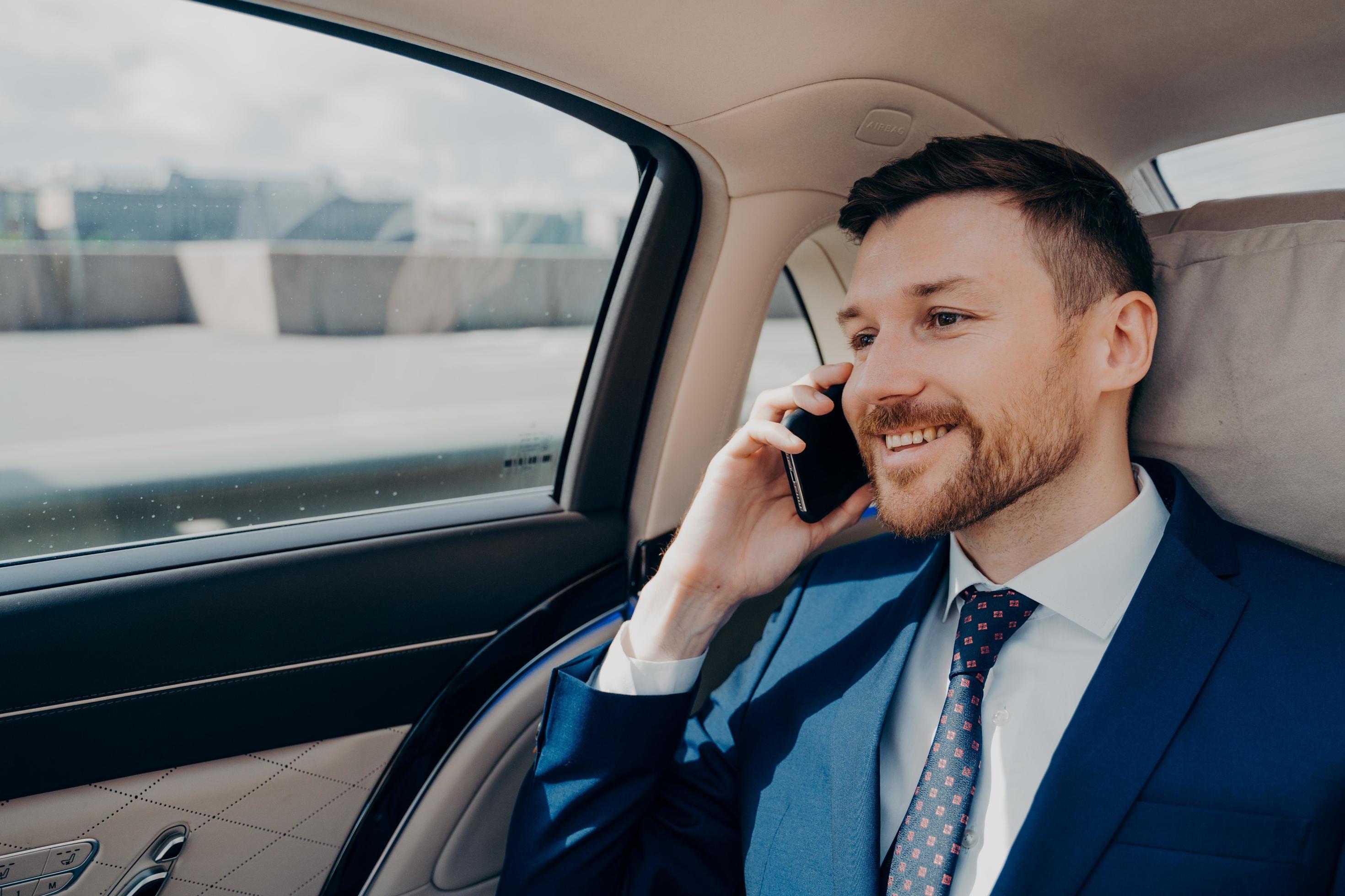 Happy business owner sitting on back seat in car and talking on phone Stock Free