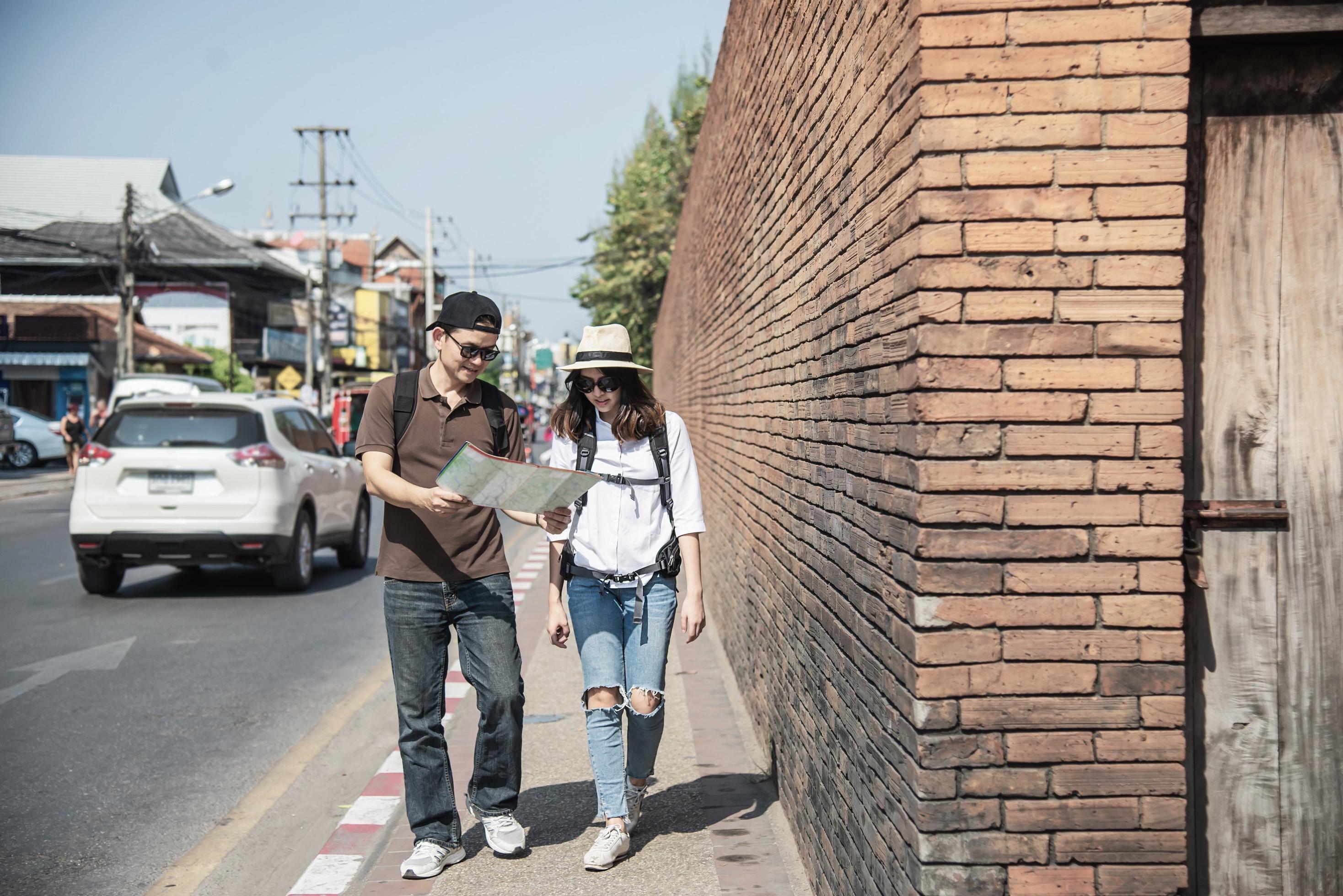 Asian backpack couple tourist holding city map crossing the road – travel people vacation lifestyle concept Stock Free