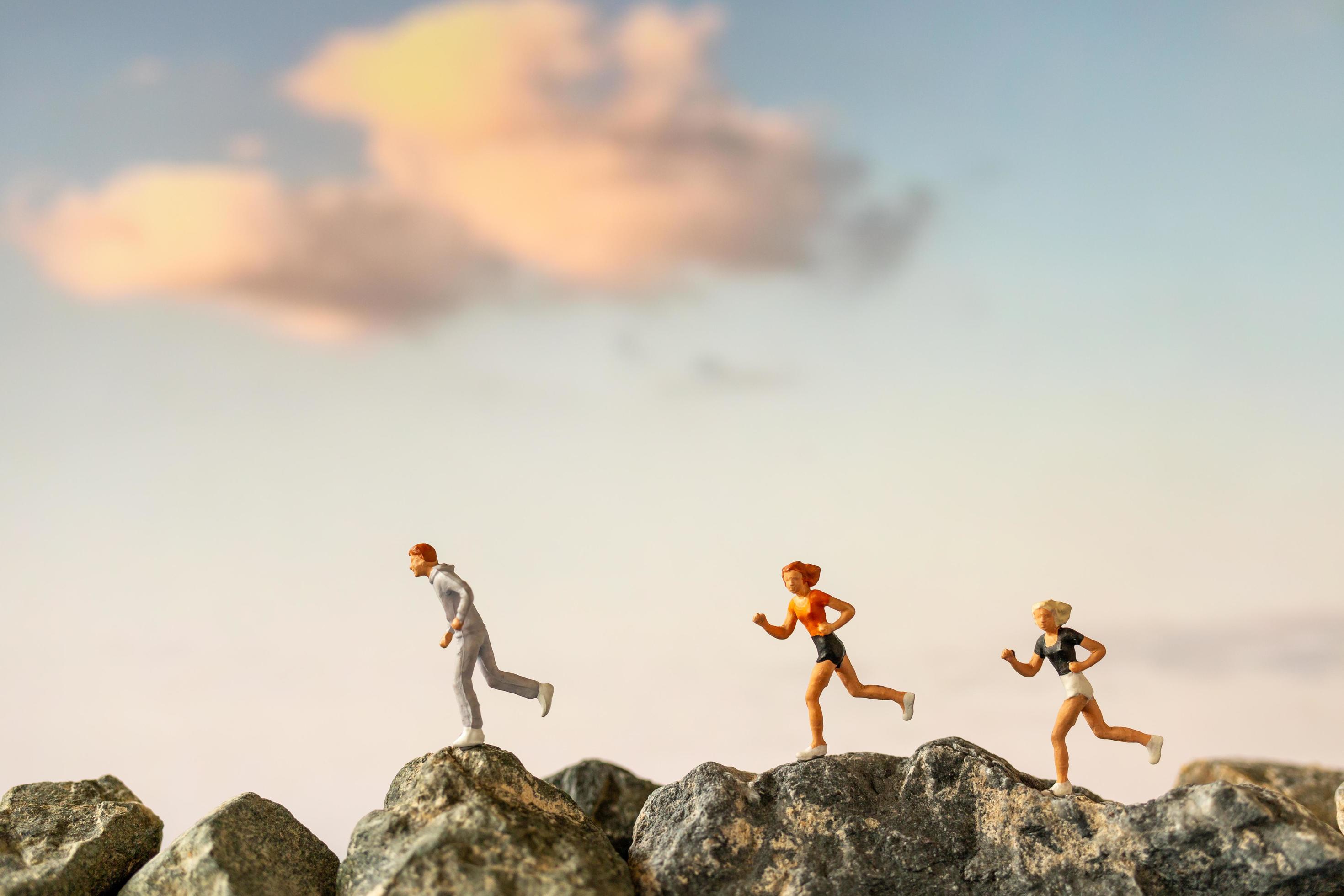 Miniature people running on a rock cliff with nature background, health and lifestyle concept Stock Free