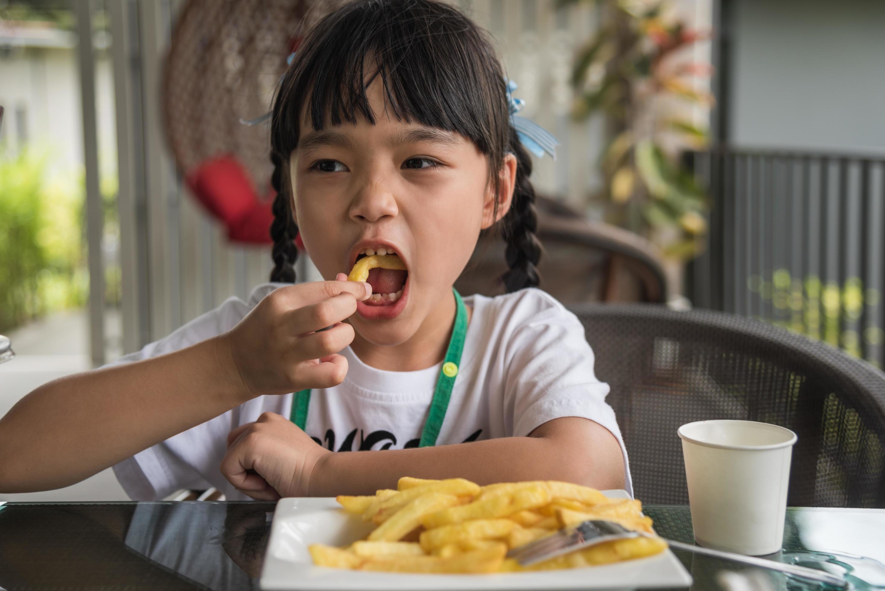 Young Asian girl eating french fries young kid fun happy potato fast food. Stock Free