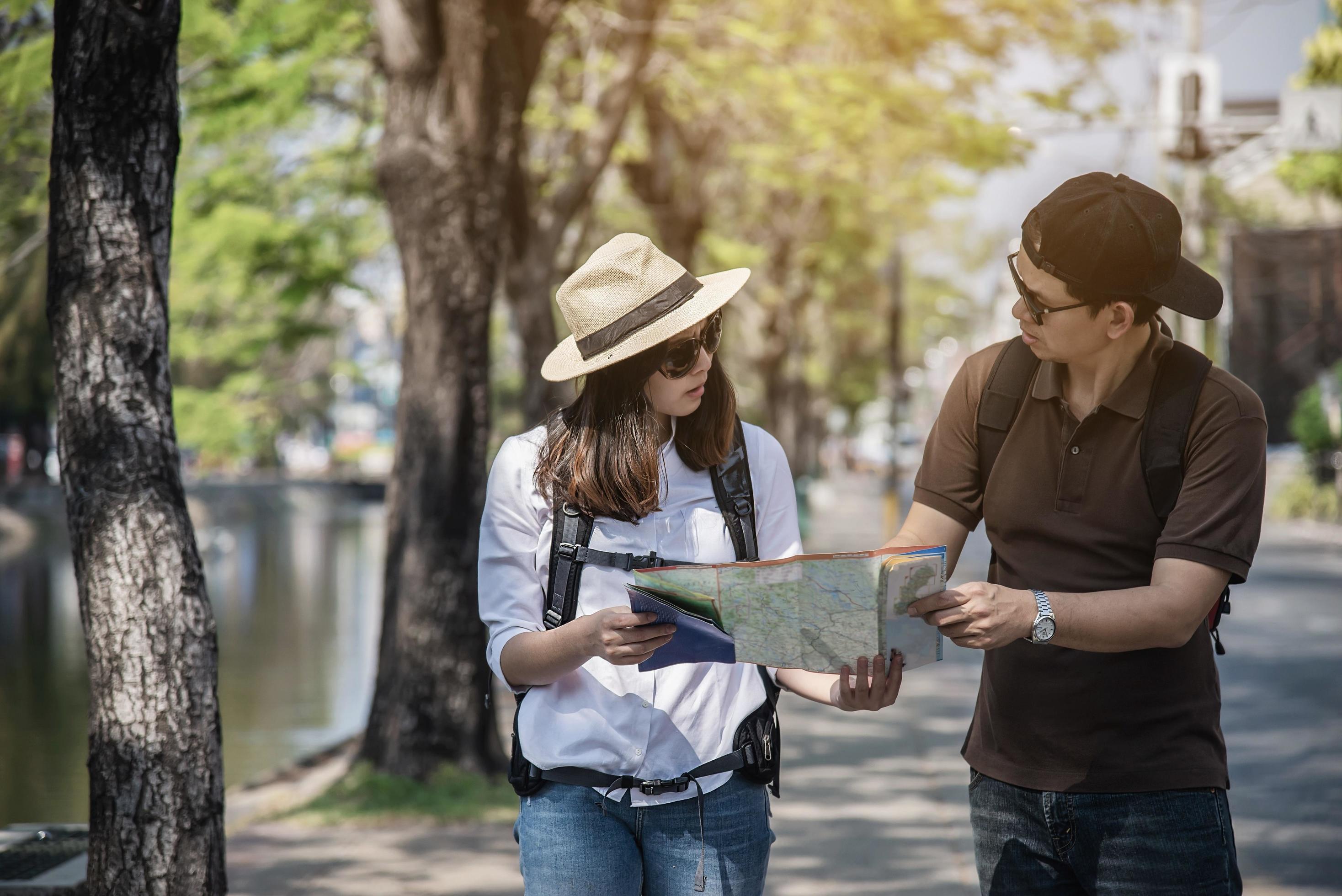 Asian backpack couple tourist holding city map crossing the road – travel people vacation lifestyle concept Stock Free