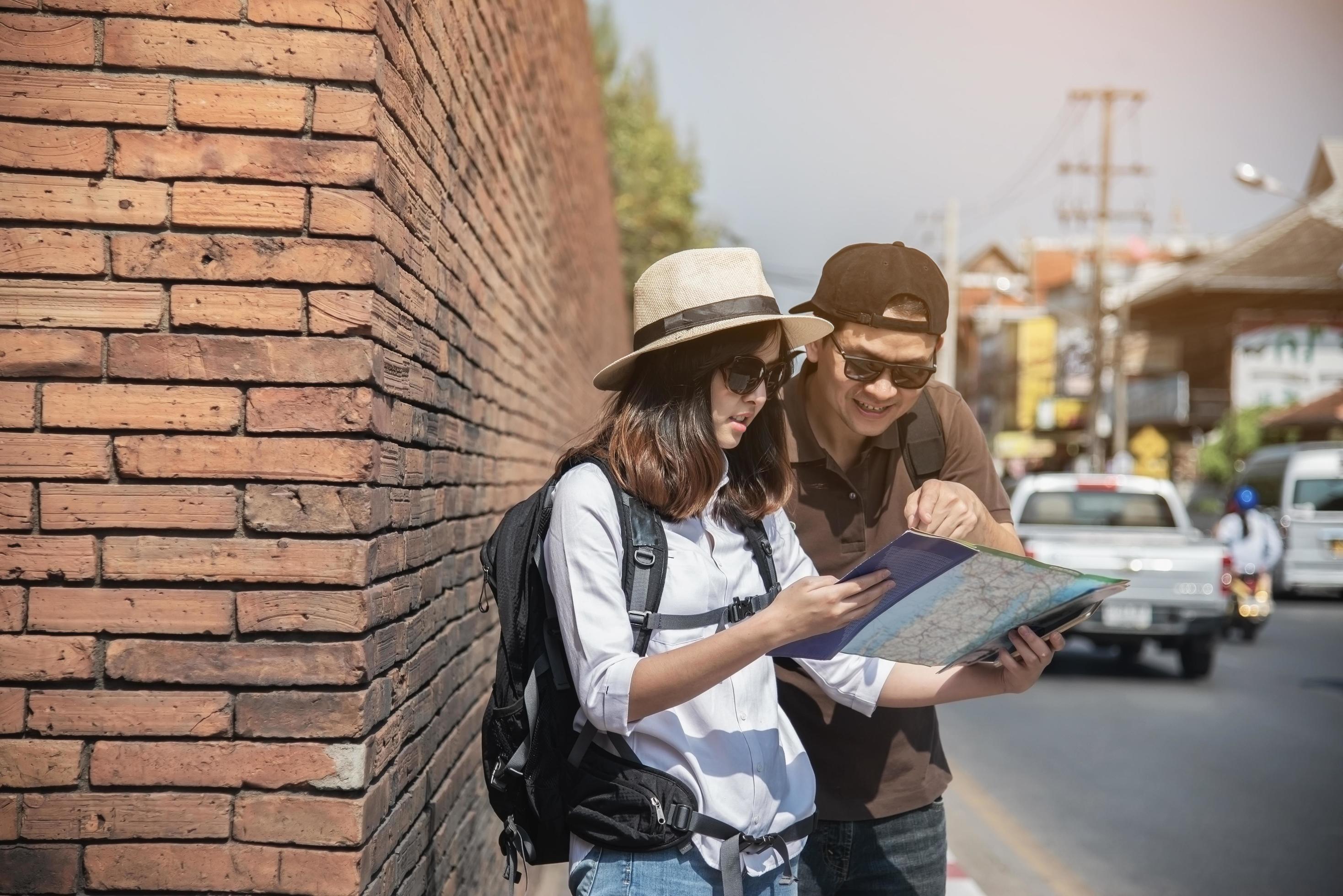 Asian backpack couple tourist holding city map crossing the road – travel people vacation lifestyle concept Stock Free