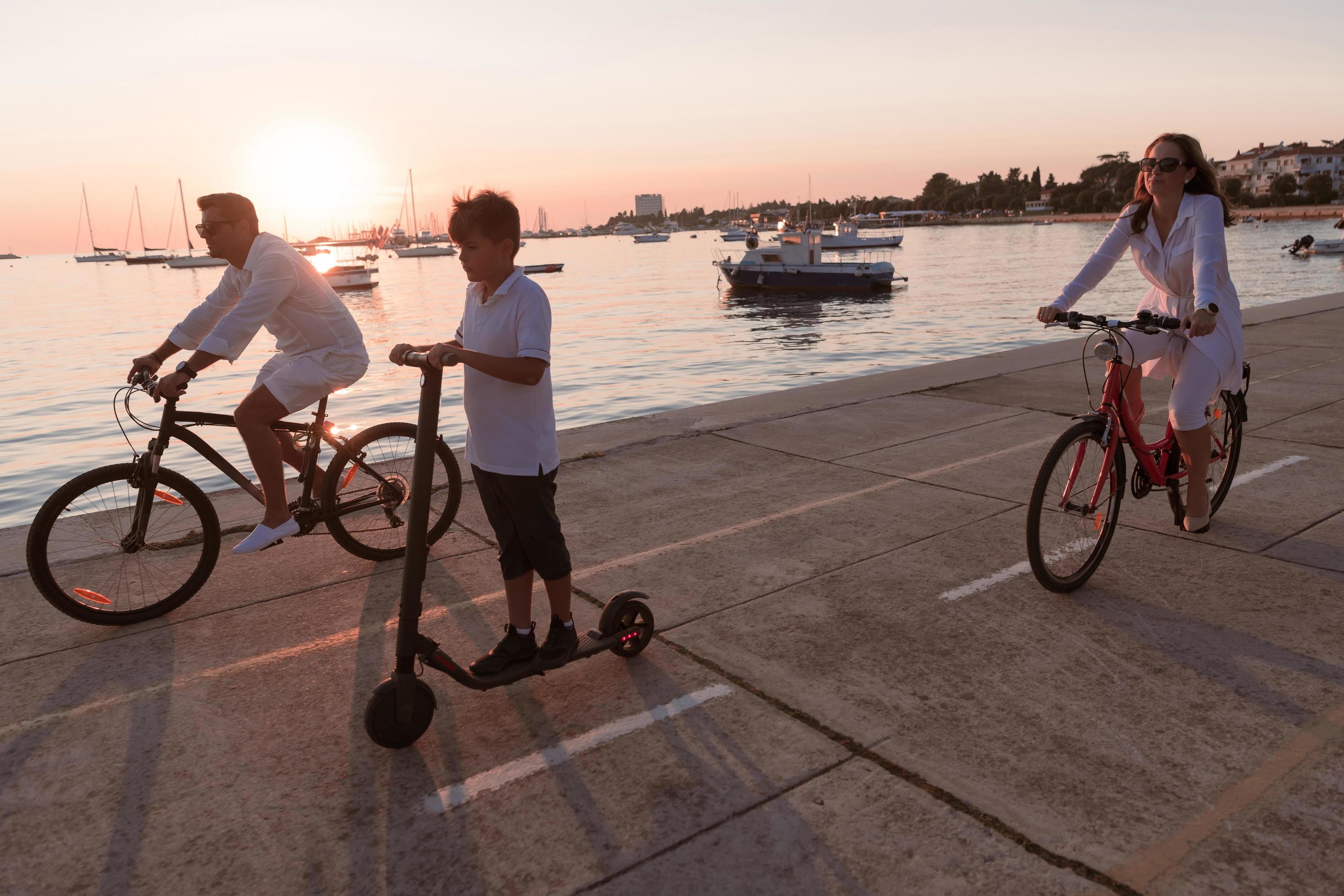 Happy family enjoying a beautiful morning by the sea together, parents riding a bike and their son riding an electric scooter. Selective focus Stock Free