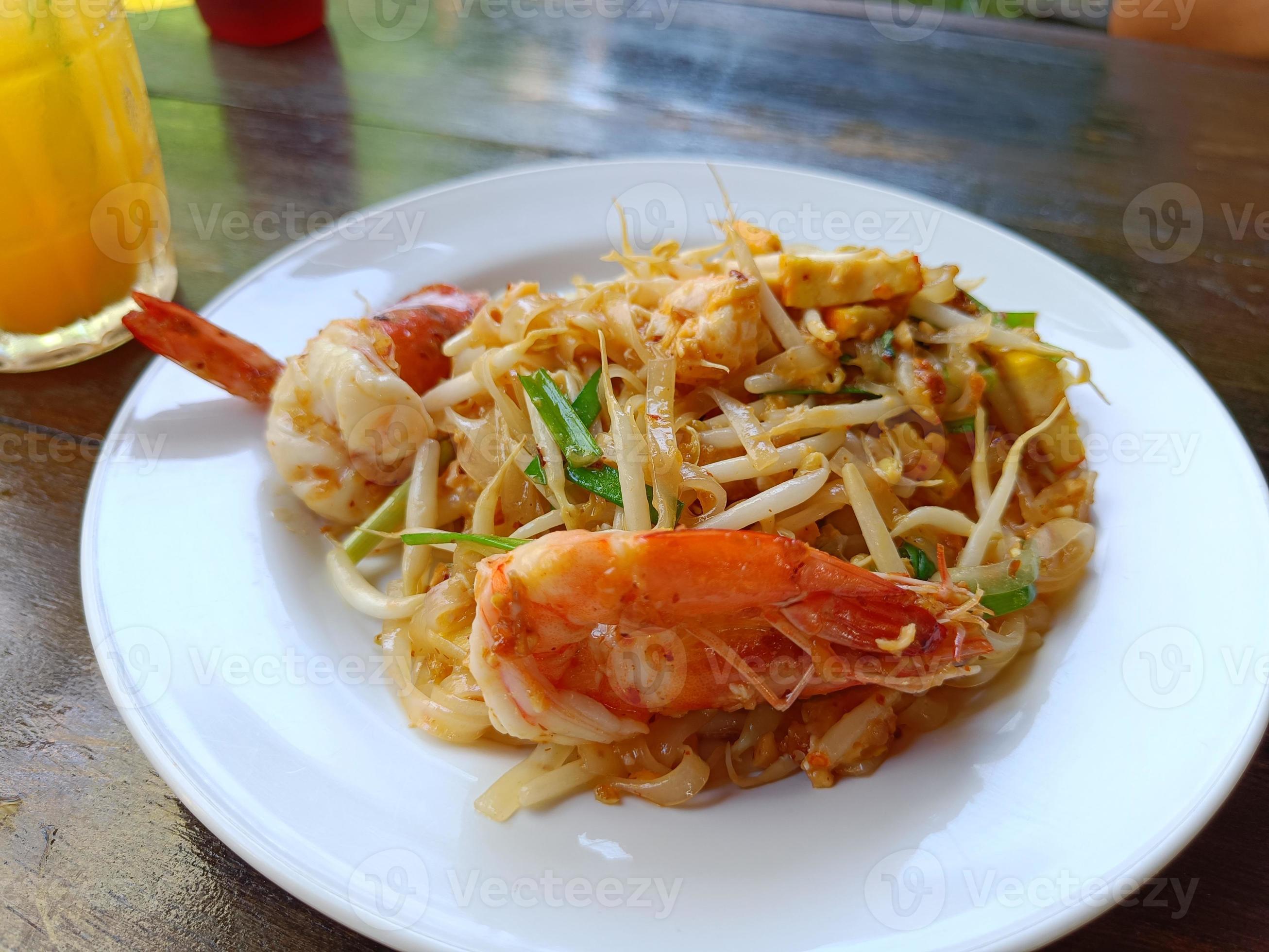 Pad Thai with fresh shrimp on a white plate on the brown table popular Thai food Stock Free