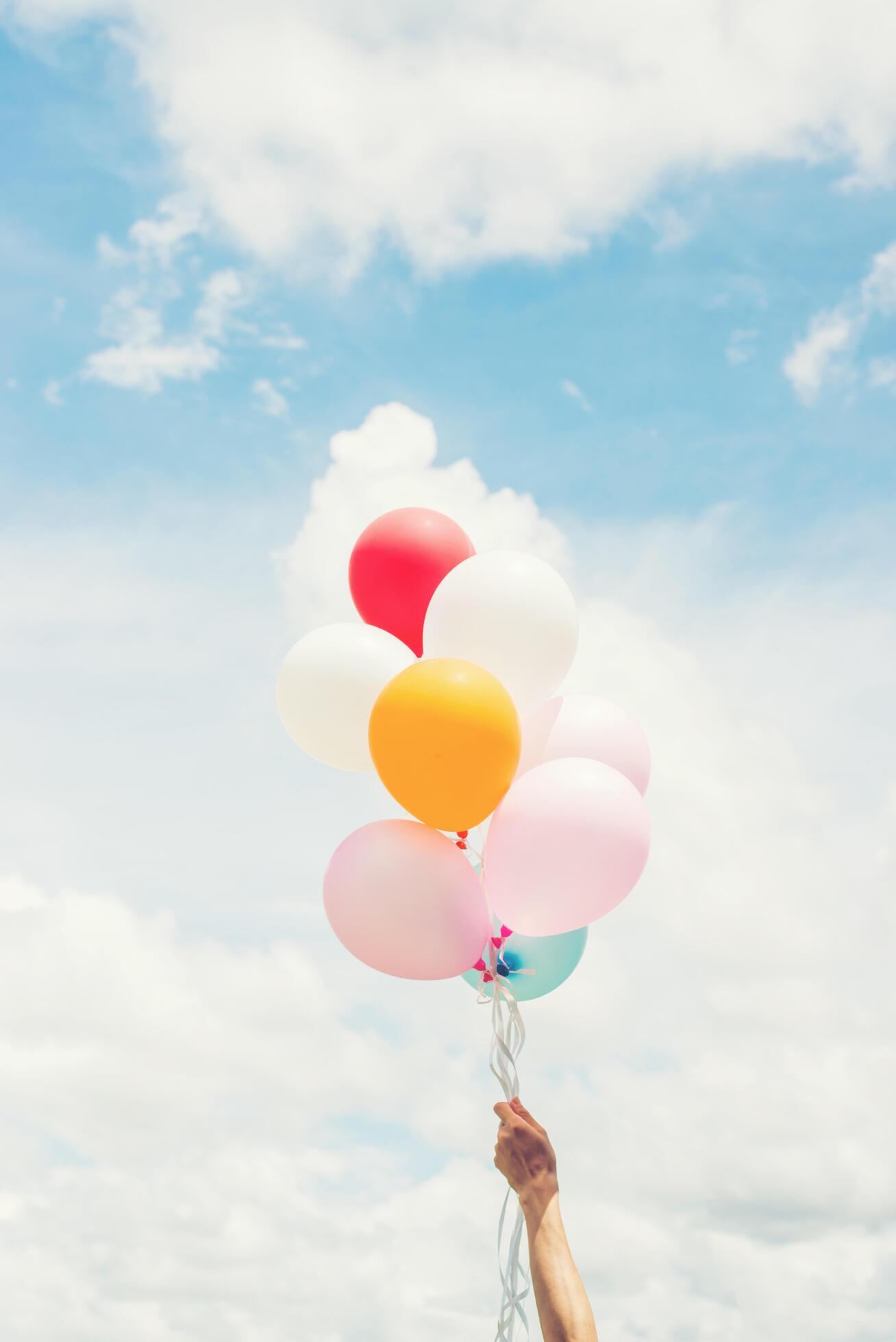 Woman Lifestyle concept woman hand holding a bunch of colored balloons with blue sky. Stock Free