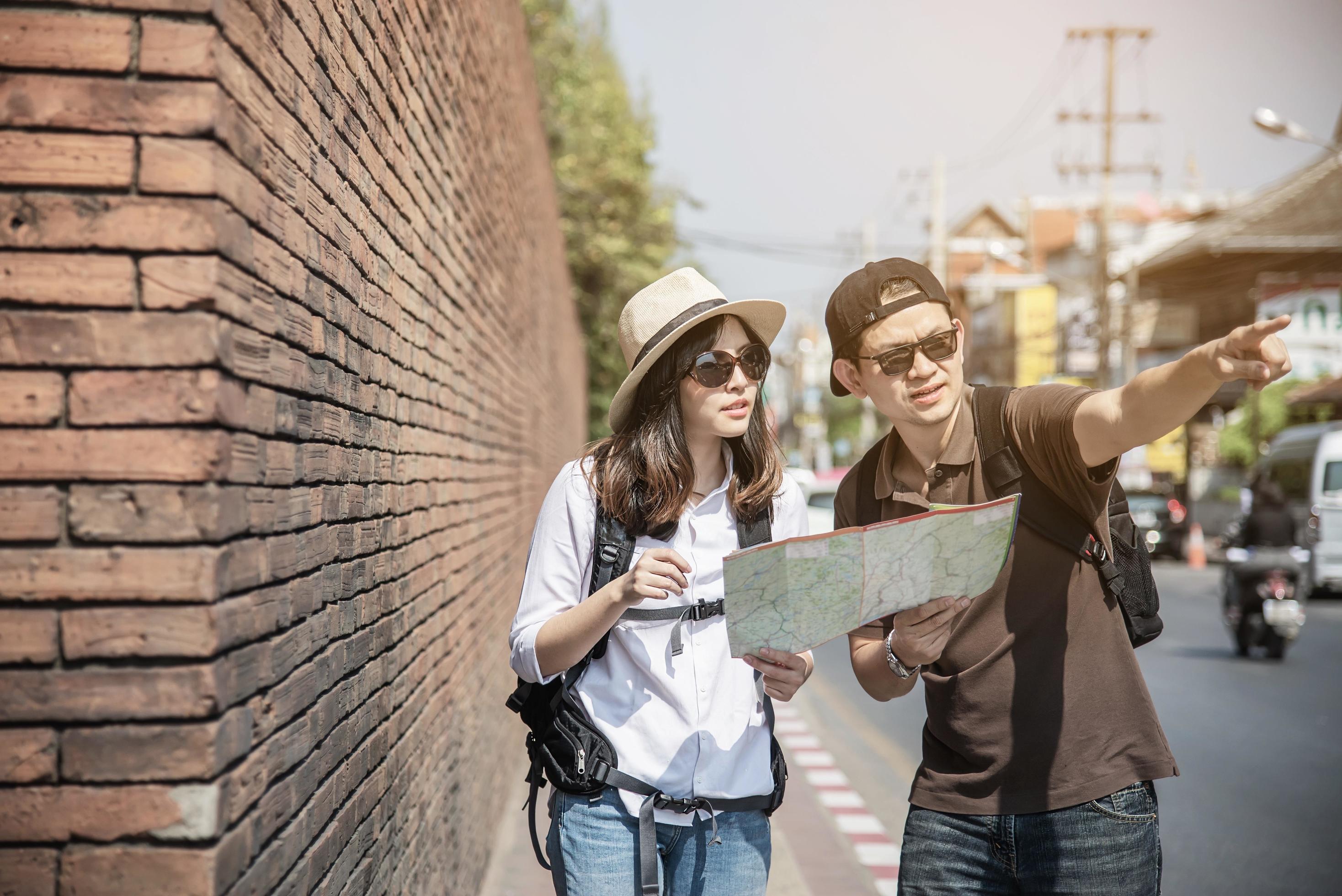 Asian backpack couple tourist holding city map crossing the road – travel people vacation lifestyle concept Stock Free