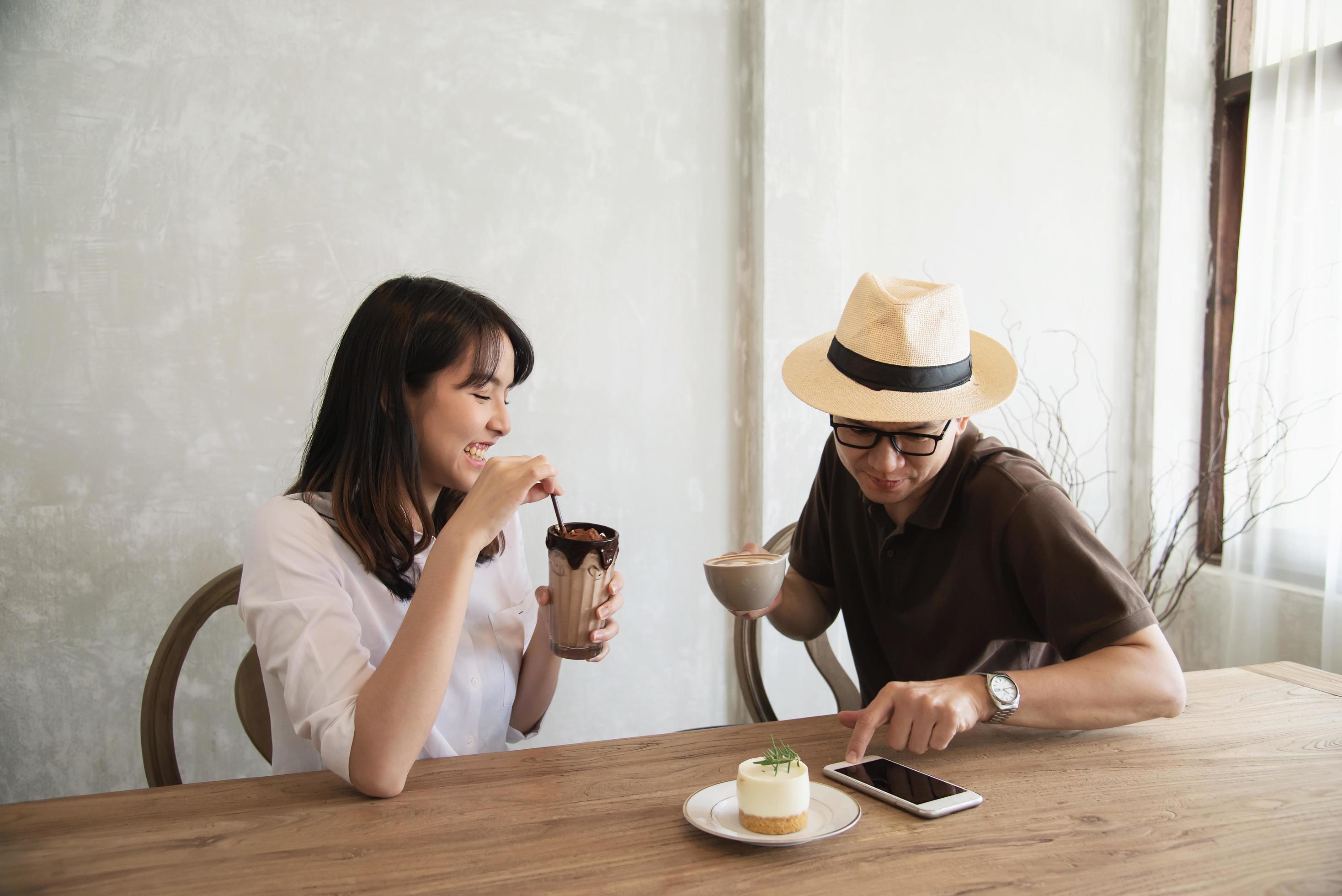 Casual man and woman talking happily while drink coffee and looking mobile phone – happy time lifestyle in coffee shop Stock Free