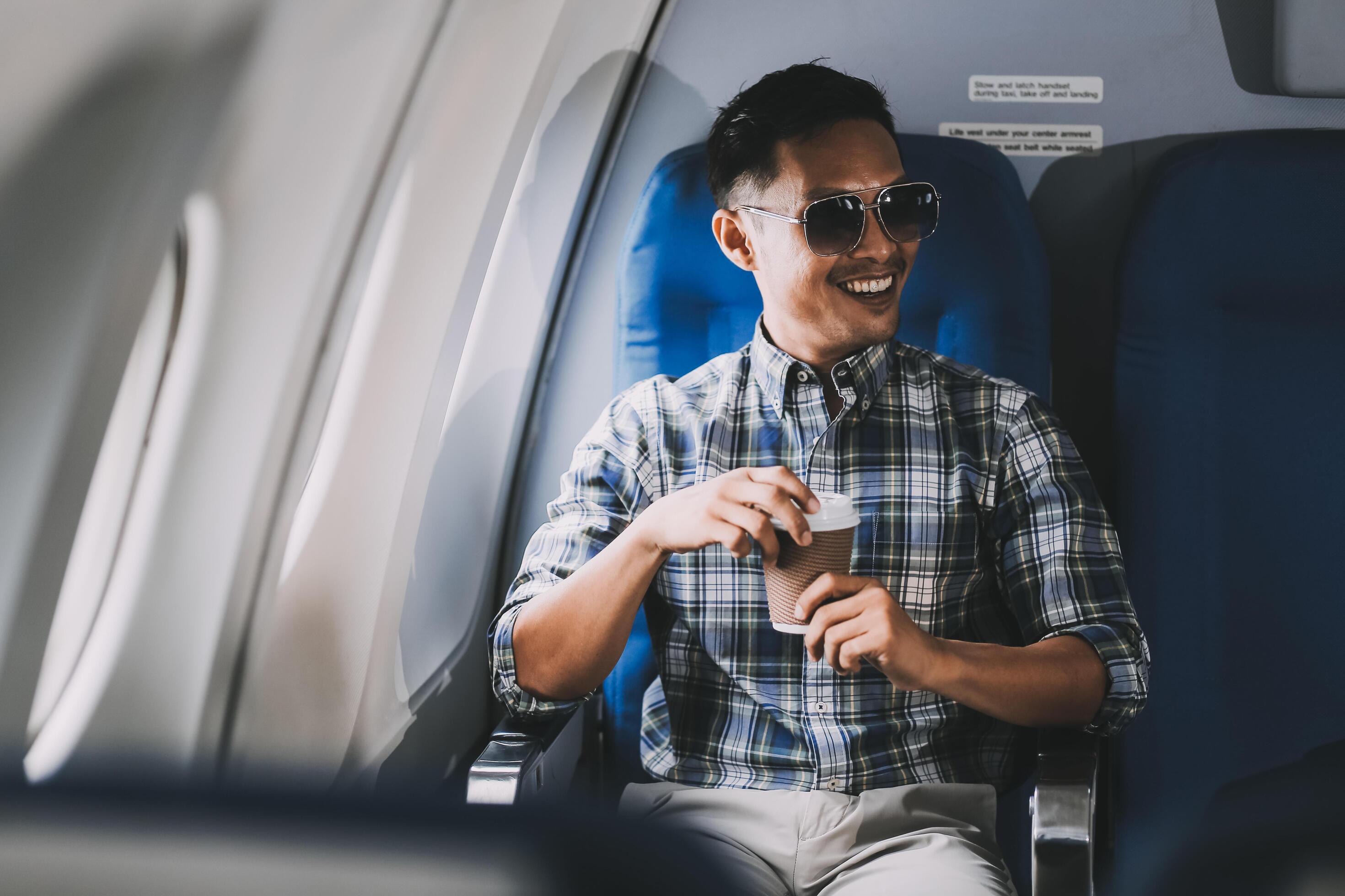 Asian man enjoying enjoys a coffee comfortable flight while sitting in the airplane cabin, Passengers near the window. Stock Free