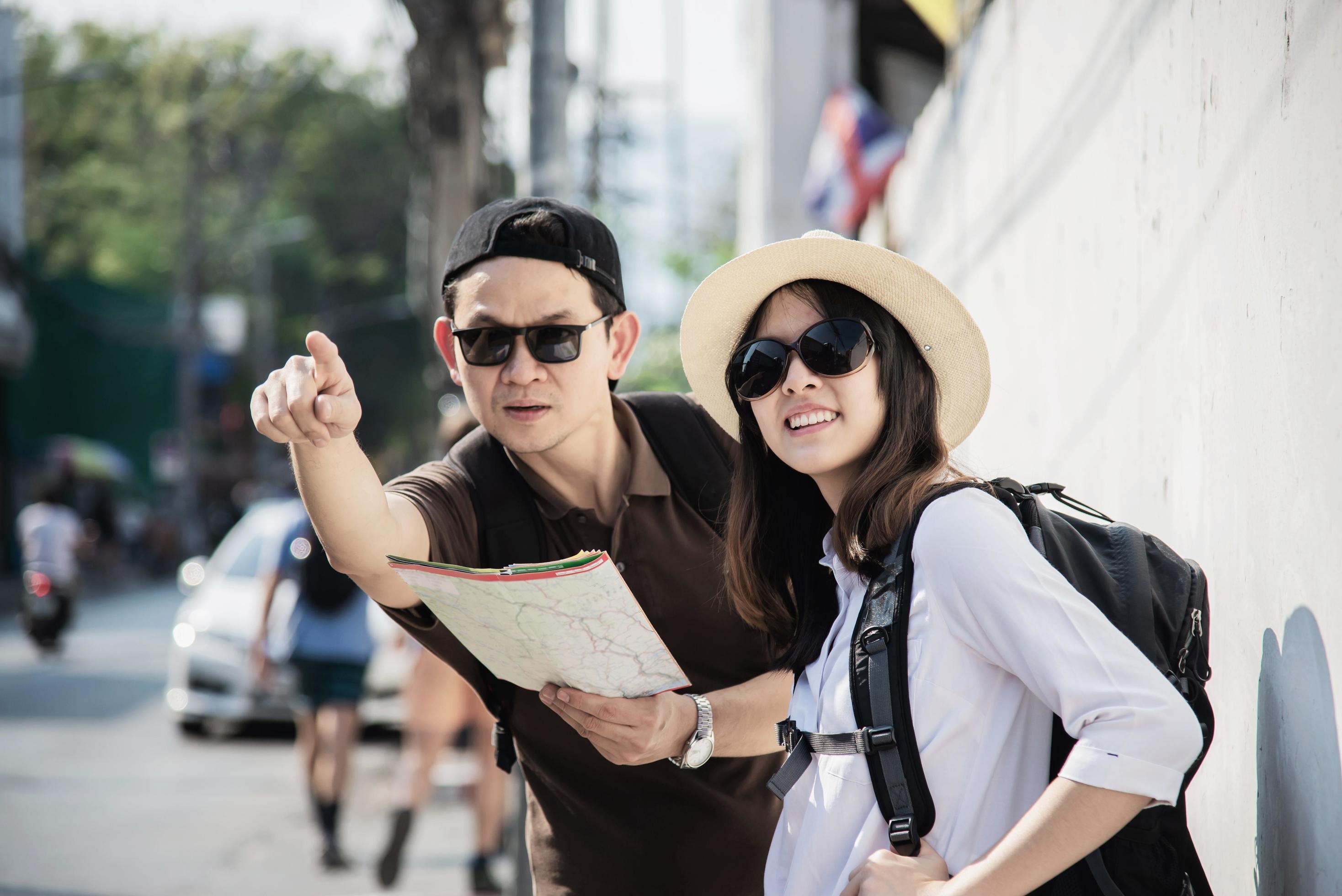 Asian backpack couple tourist holding city map crossing the road – travel people vacation lifestyle concept Stock Free