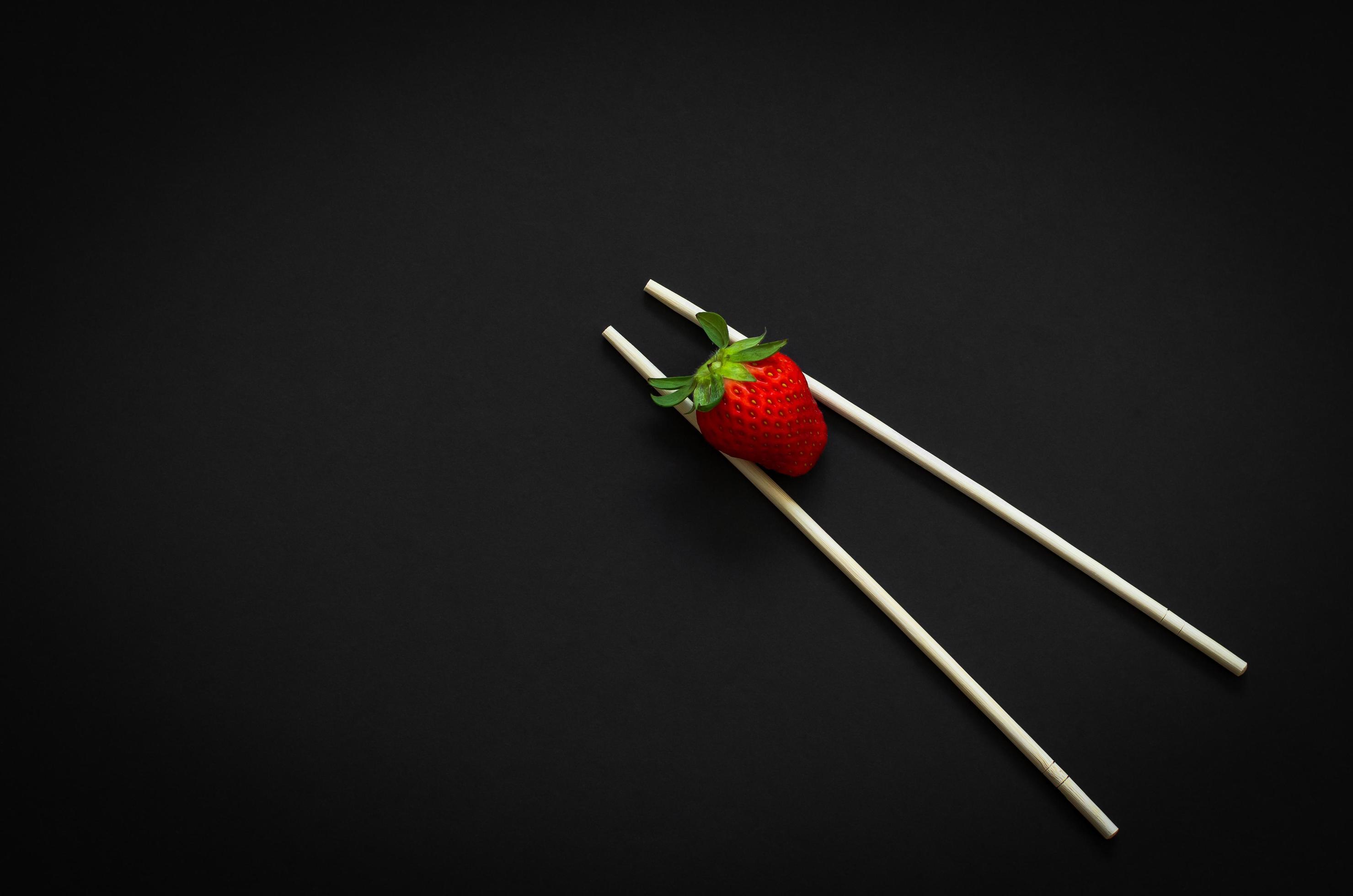 Strawberry and chopsticks on dark background for minimalist flat lay black food concept. Stock Free