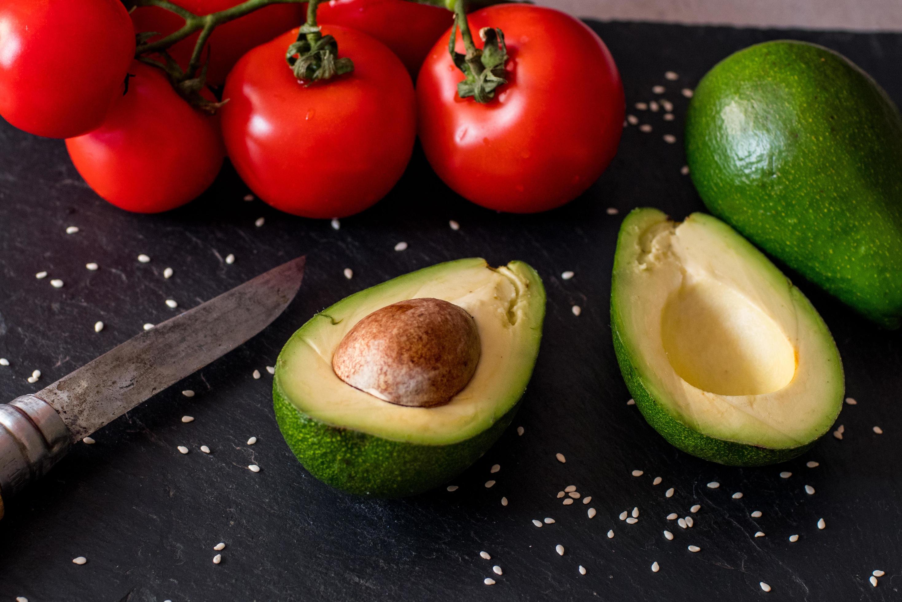 Tomatos and avocado on black table close up, colorful healthy food Stock Free