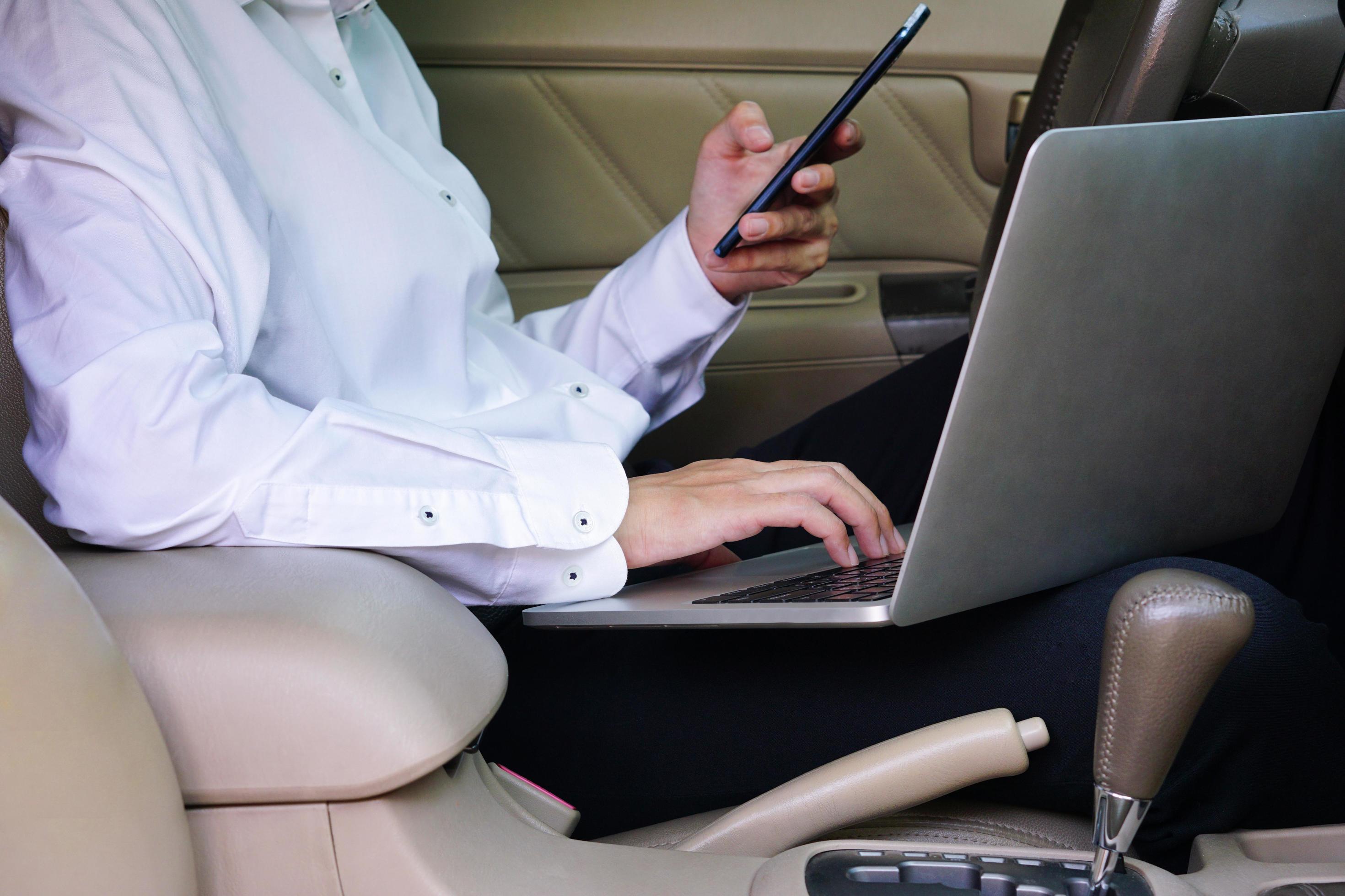 Businessman working on laptop and mobile phone while sitting on driver seat in car. Lifestyle concept. Stock Free