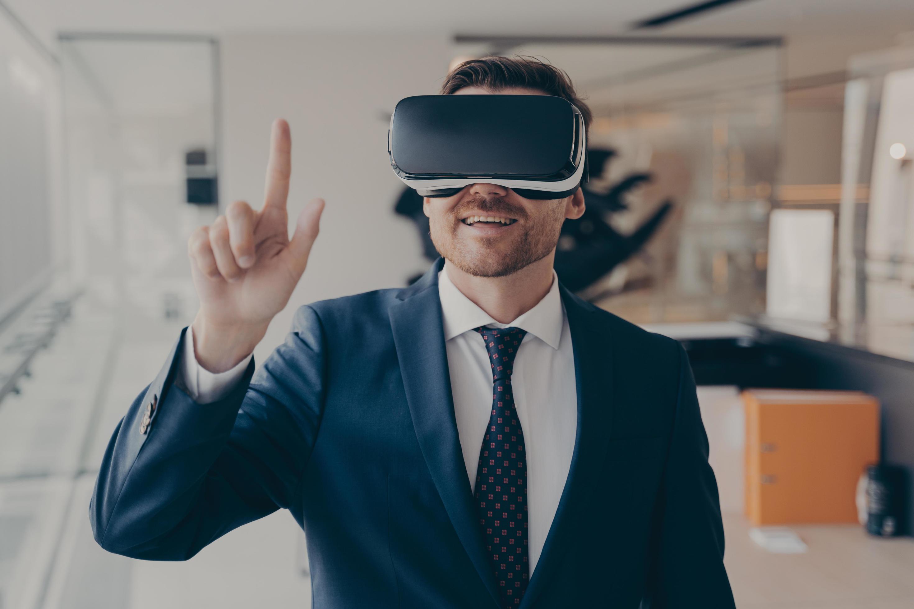 
									Young successful businessman in VR goggles touching air with finger during virtual business meeting Stock Free