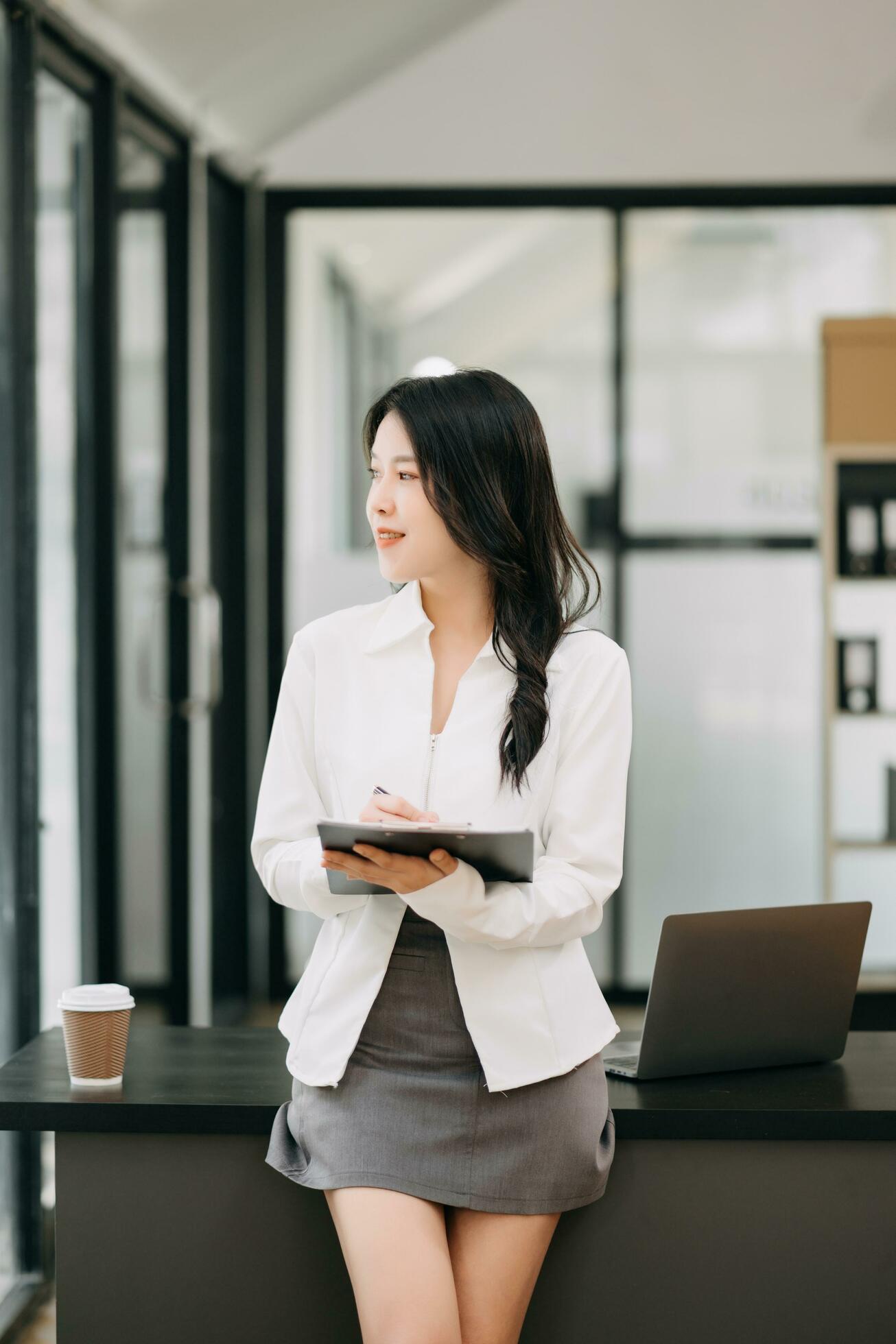 Confident business expert attractive smiling young asian woman holding digital tablet and laptop on desk in office. Stock Free