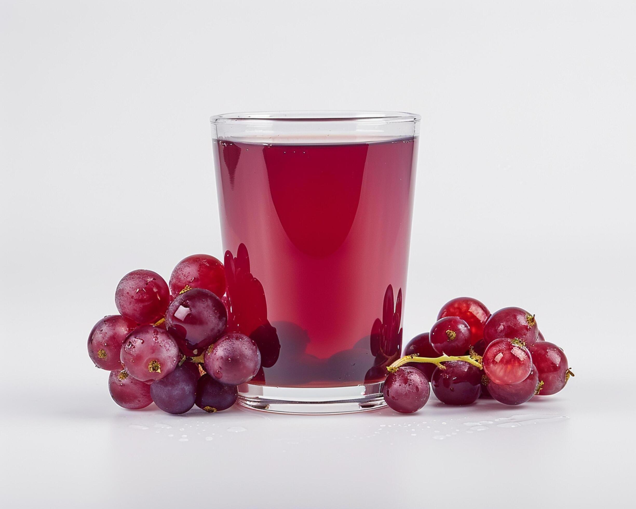 a glass of red grape juice with some grapes Stock Free