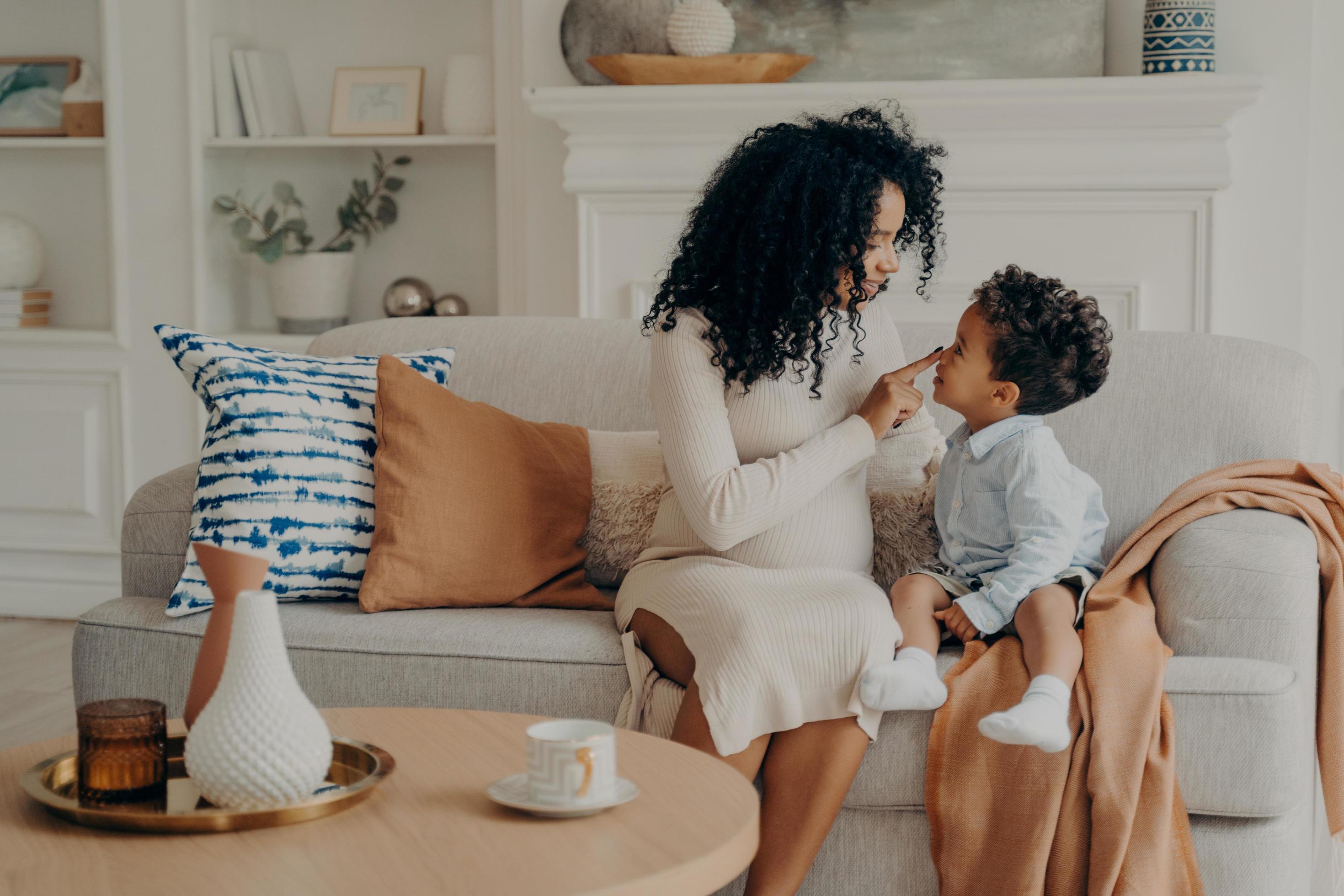 Portrait of beautiful family pregnant mother and son afro ethnic race sitting on sofa Stock Free