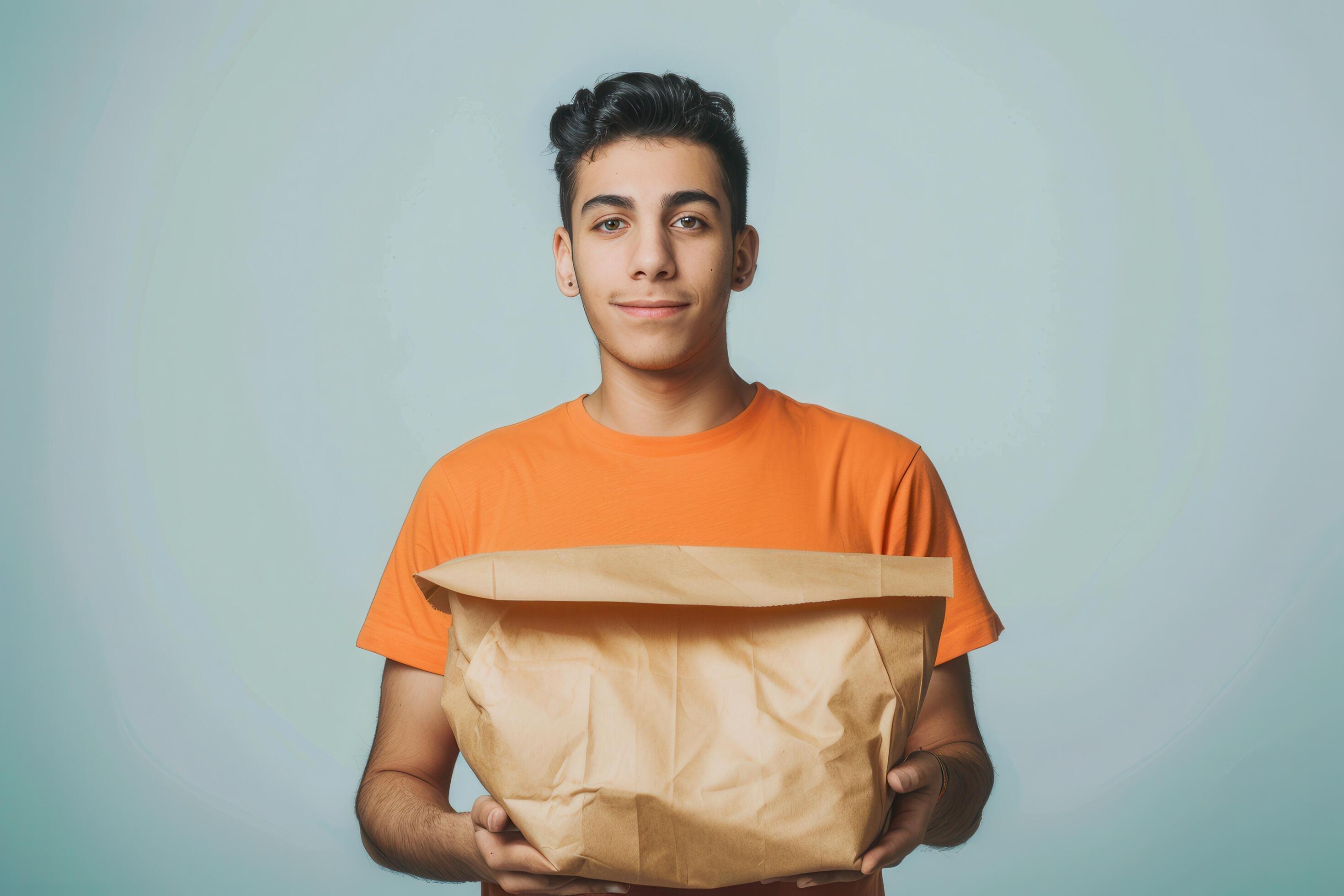 Young Man Holding a Brown Paper Bag in Front of a Light Blue Background Stock Free