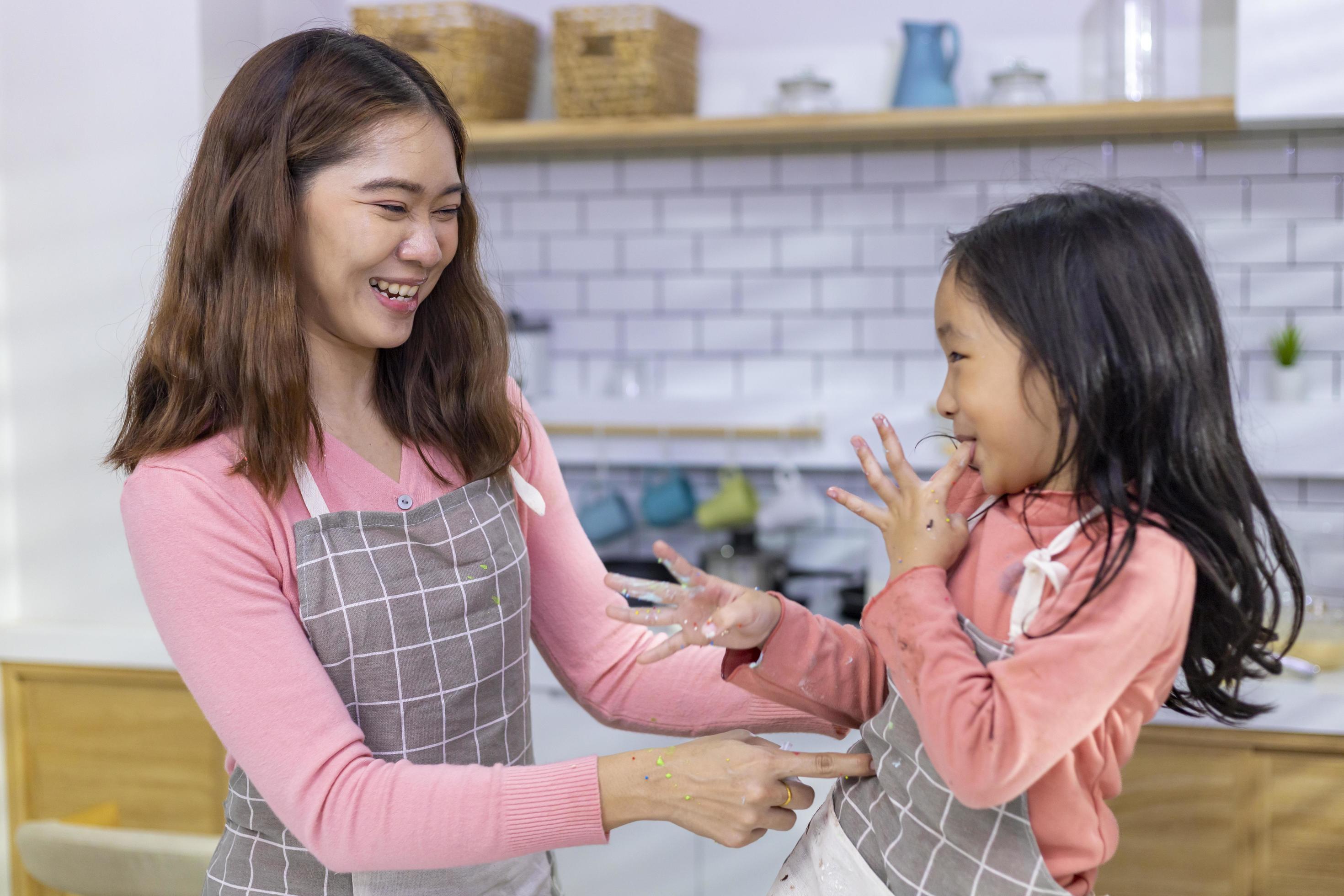 Happy Asian mother is tickling her daughter for having fun time after cooking in the kitchen for love and family concept Stock Free