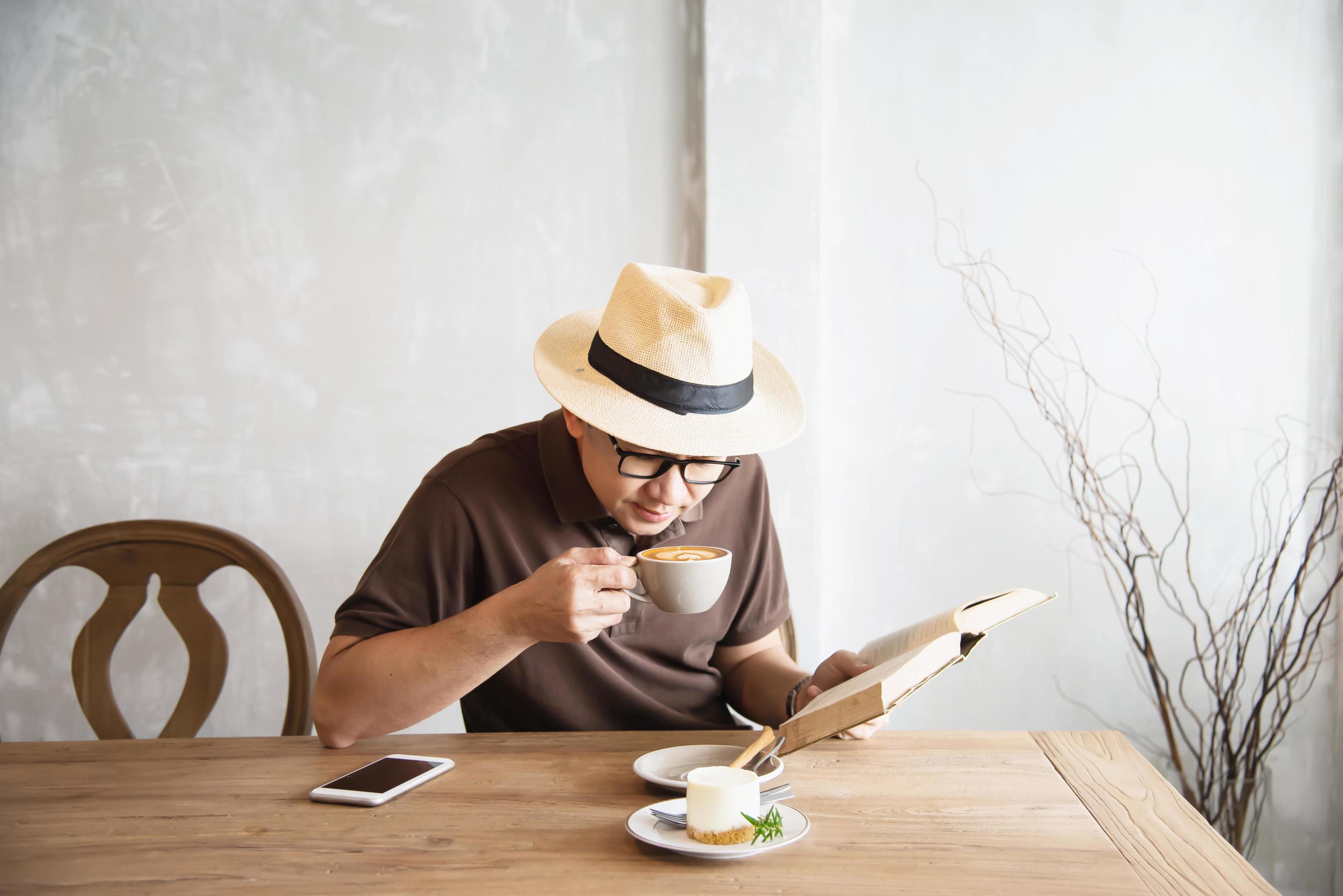 Relax Asian man drink coffee and read book in a modern style coffee shop – people with coffee cup easy lifestyle concept Stock Free