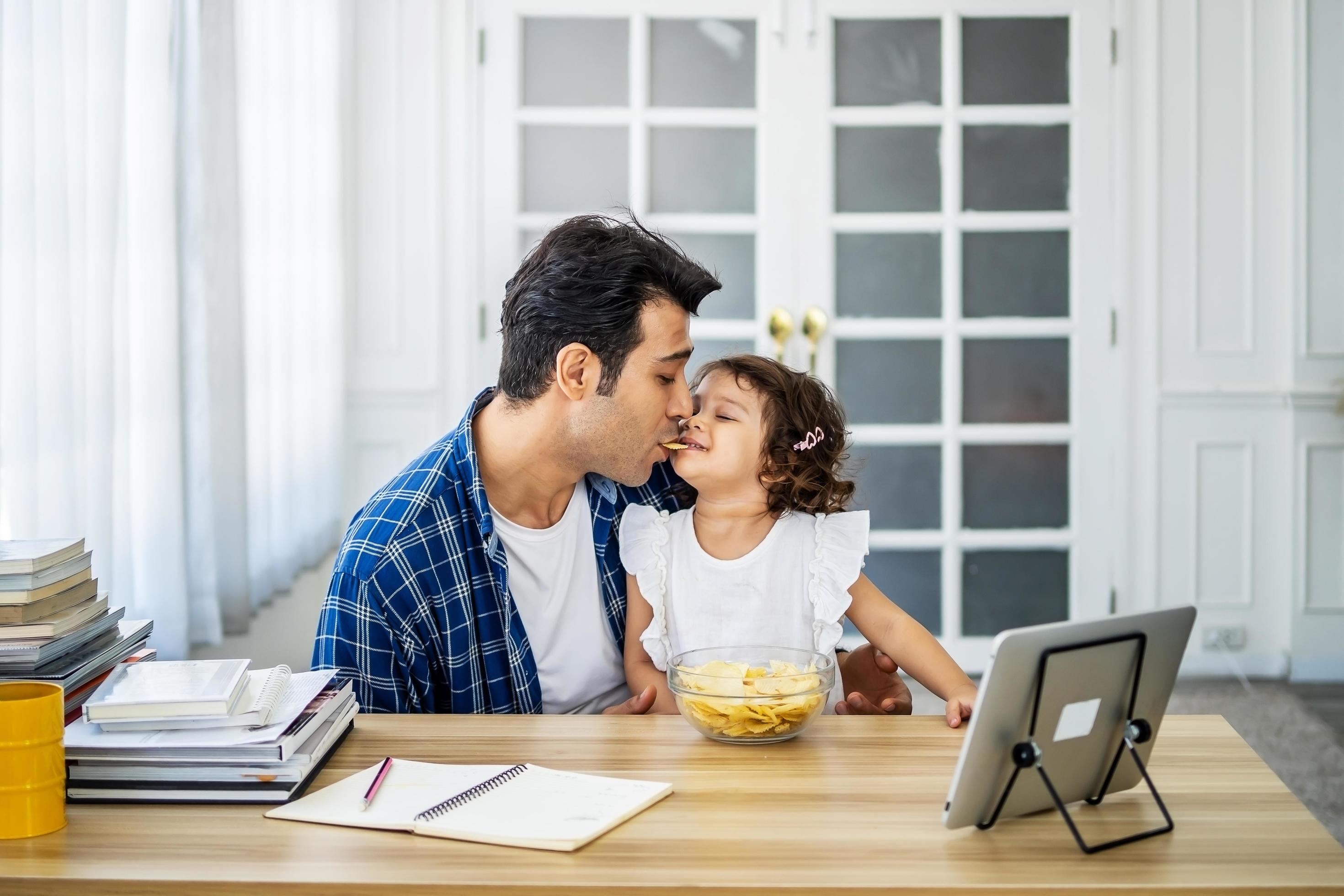 Caucasian family young father eating potato chips in mounth with little daughter together and watch cartoons educational online program Stock Free