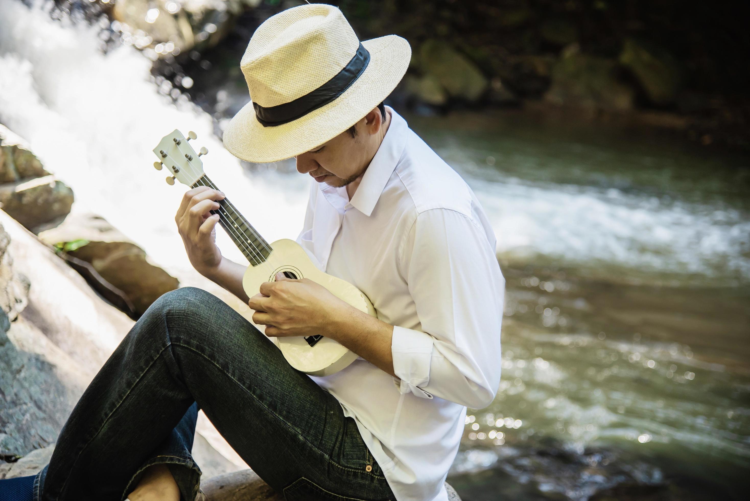 Man play ukulele new to the waterfall – people and music instrument life style in nature concept Stock Free