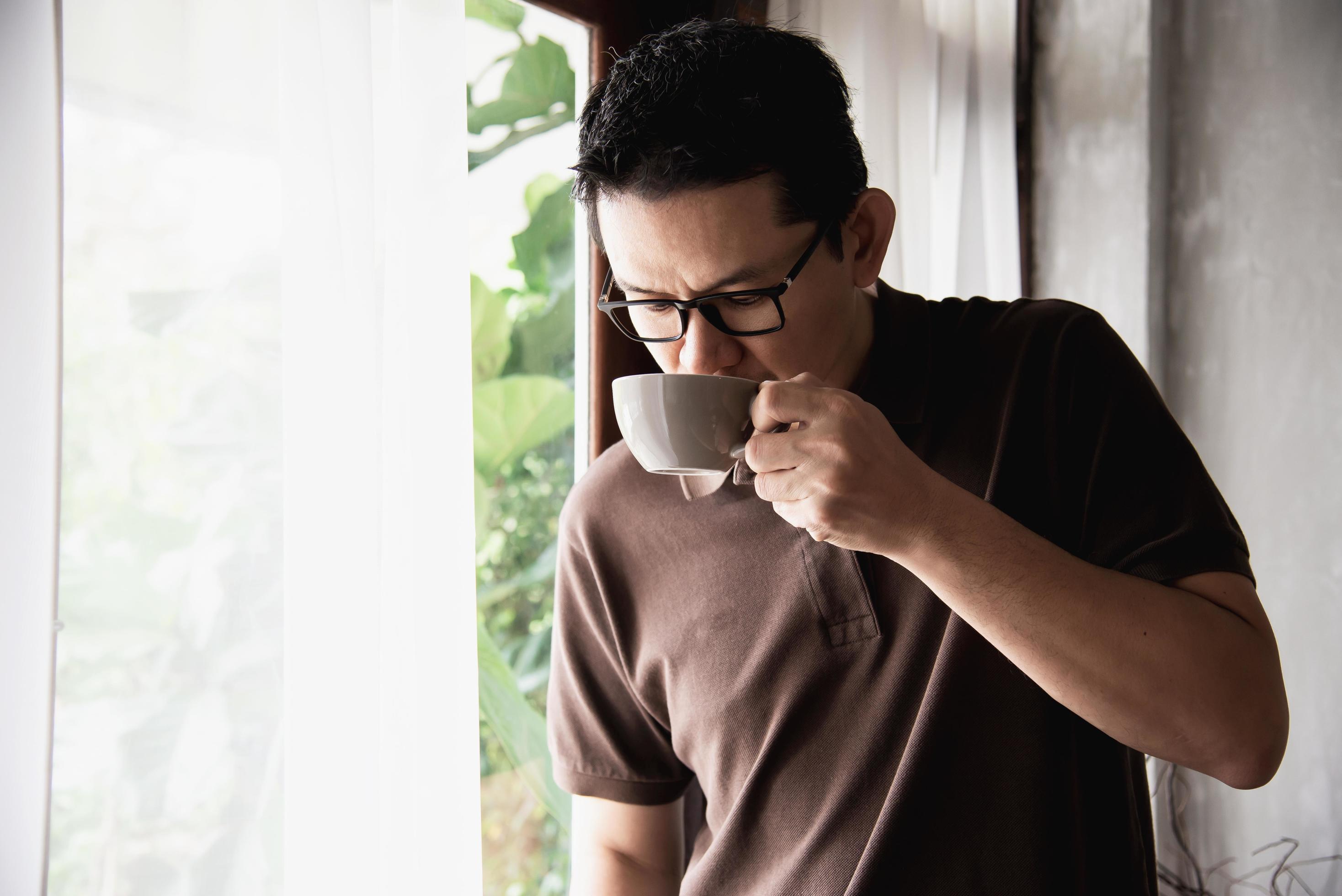 Relax Asian man drink coffee and read book in a modern style coffee shop – people with coffee cup easy lifestyle concept Stock Free