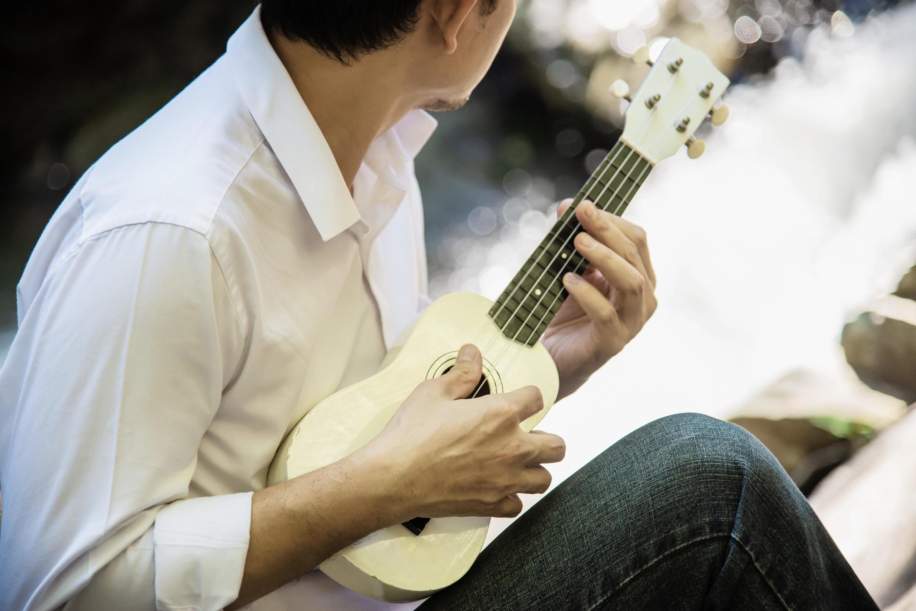 Man play ukulele new to the river- people and music instrument life style in nature concept Stock Free