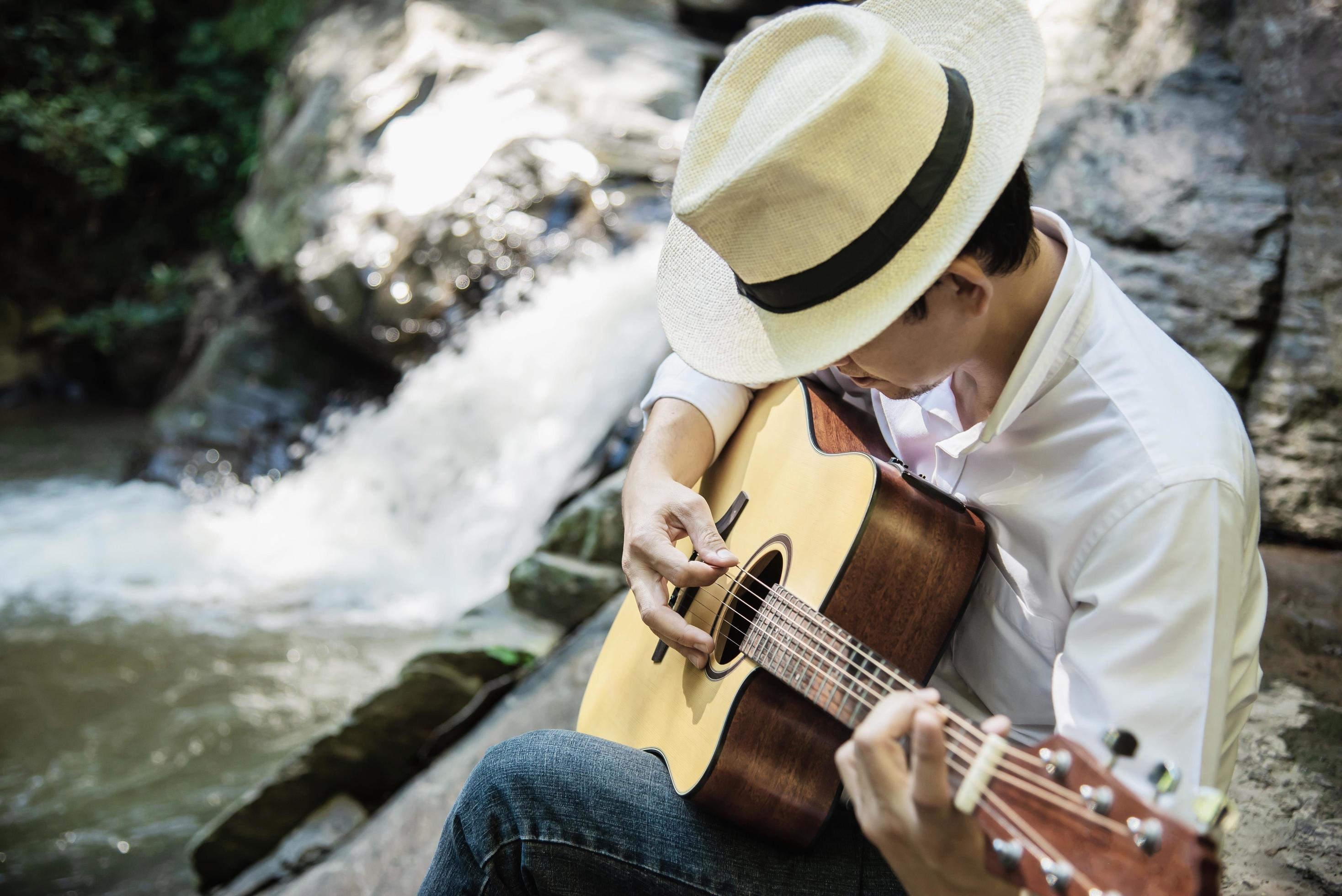 Man play guitar near to the waterfall – people and music instrument life style in nature concept Stock Free