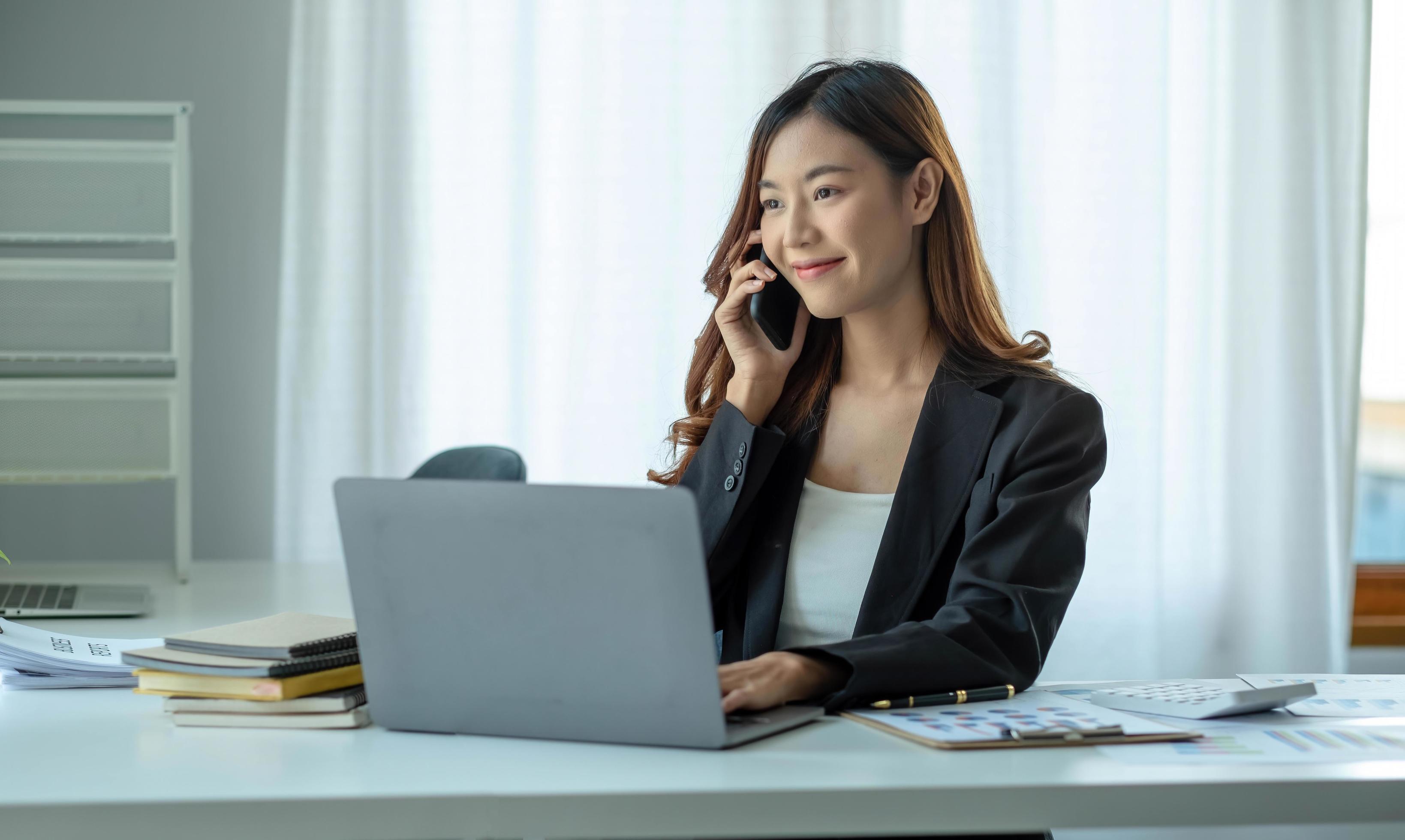 Asian business woman have the joy of talking on the phone, laptop and tablet on the office desk. Stock Free